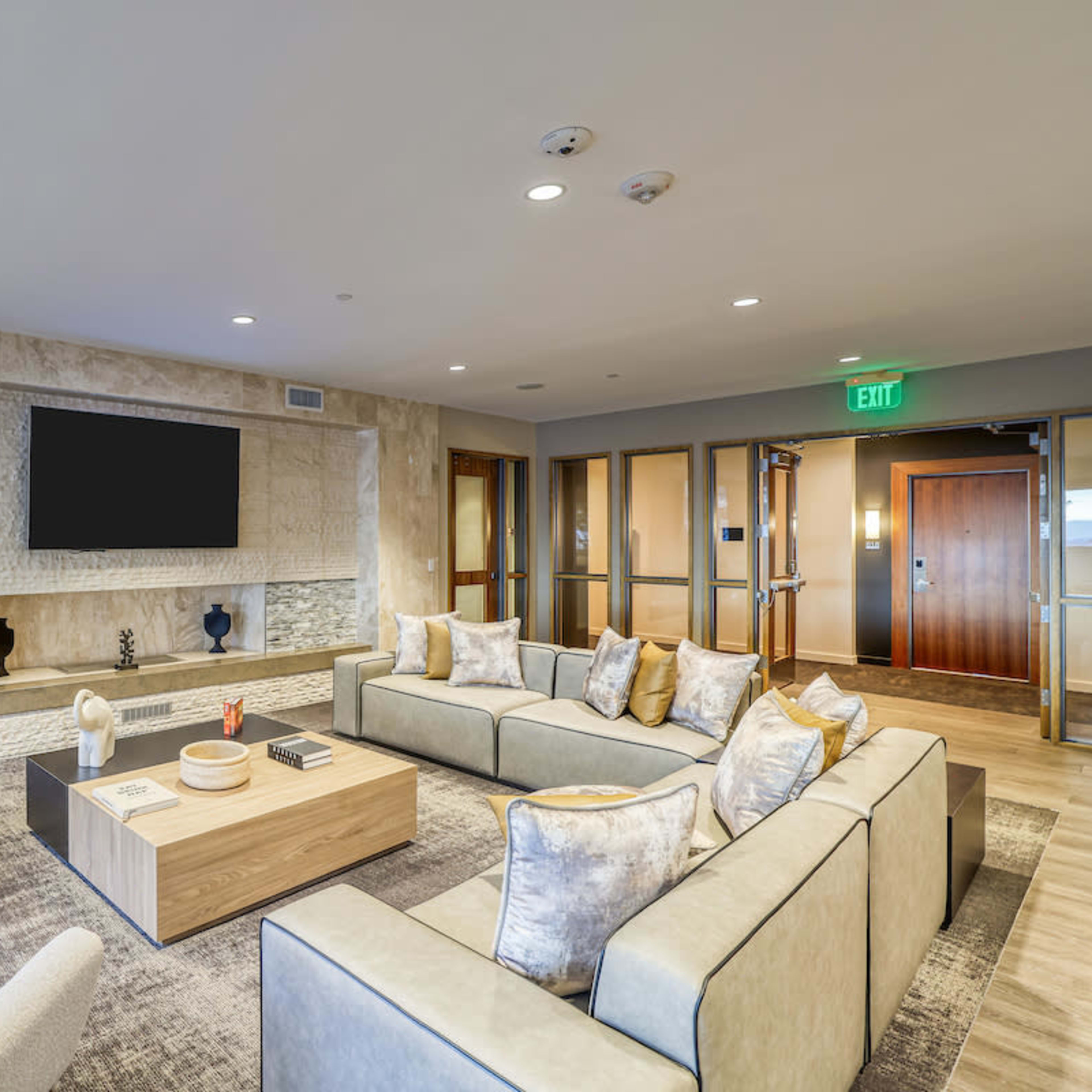 A modern lounge area with a large sectional sofa, a coffee table, an elegant light fixture, and a wall-mounted television.