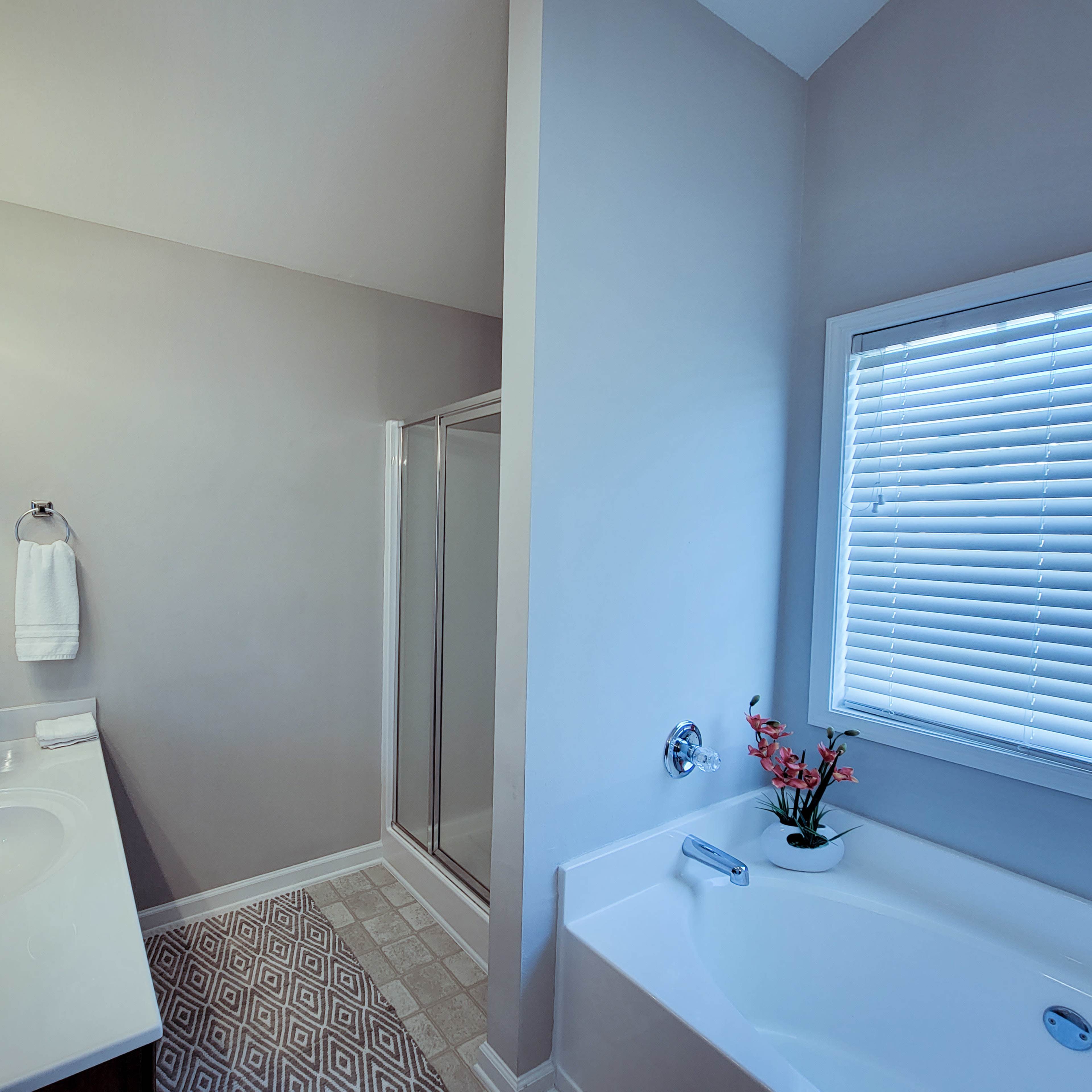 A modern bathroom featuring a double sink vanity, a shower, and a bathtub with a small flower arrangement on the edge.