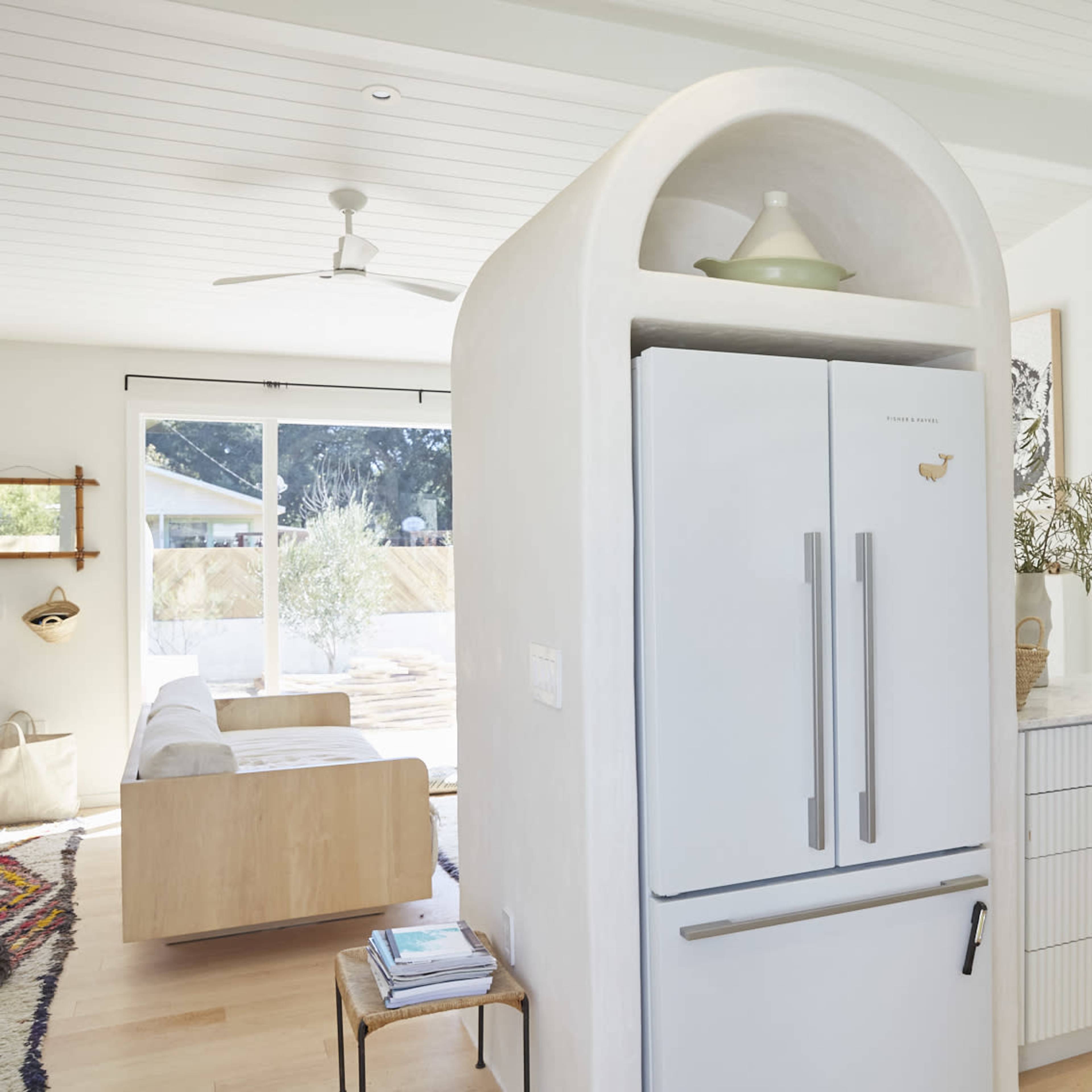 A modern kitchen featuring a curved refrigerator, a white countertop, and a spacious sitting area with a large window letting in natural light.