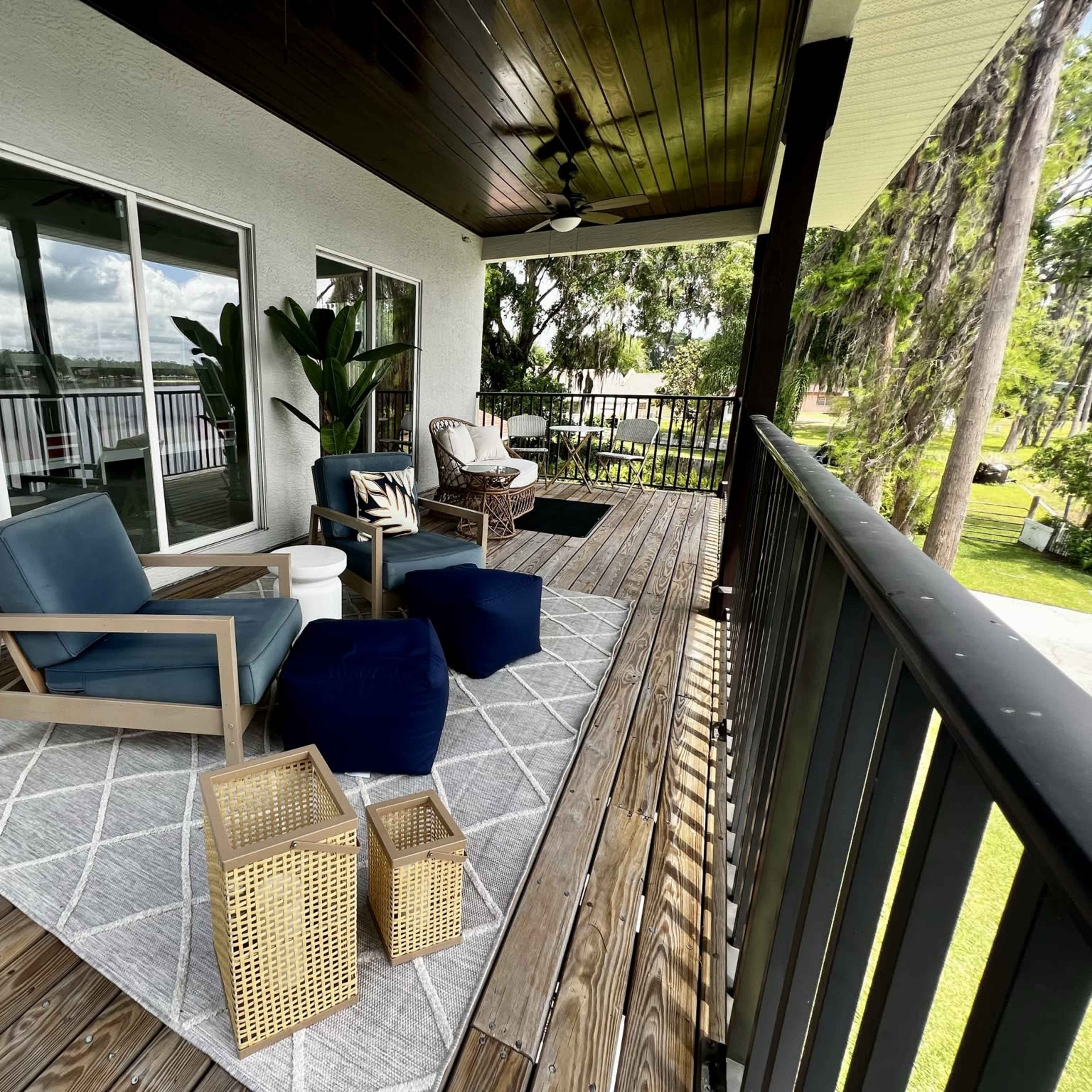 A well-furnished outdoor balcony with comfortable seating, a patterned rug, and decorative tables surrounded by greenery.