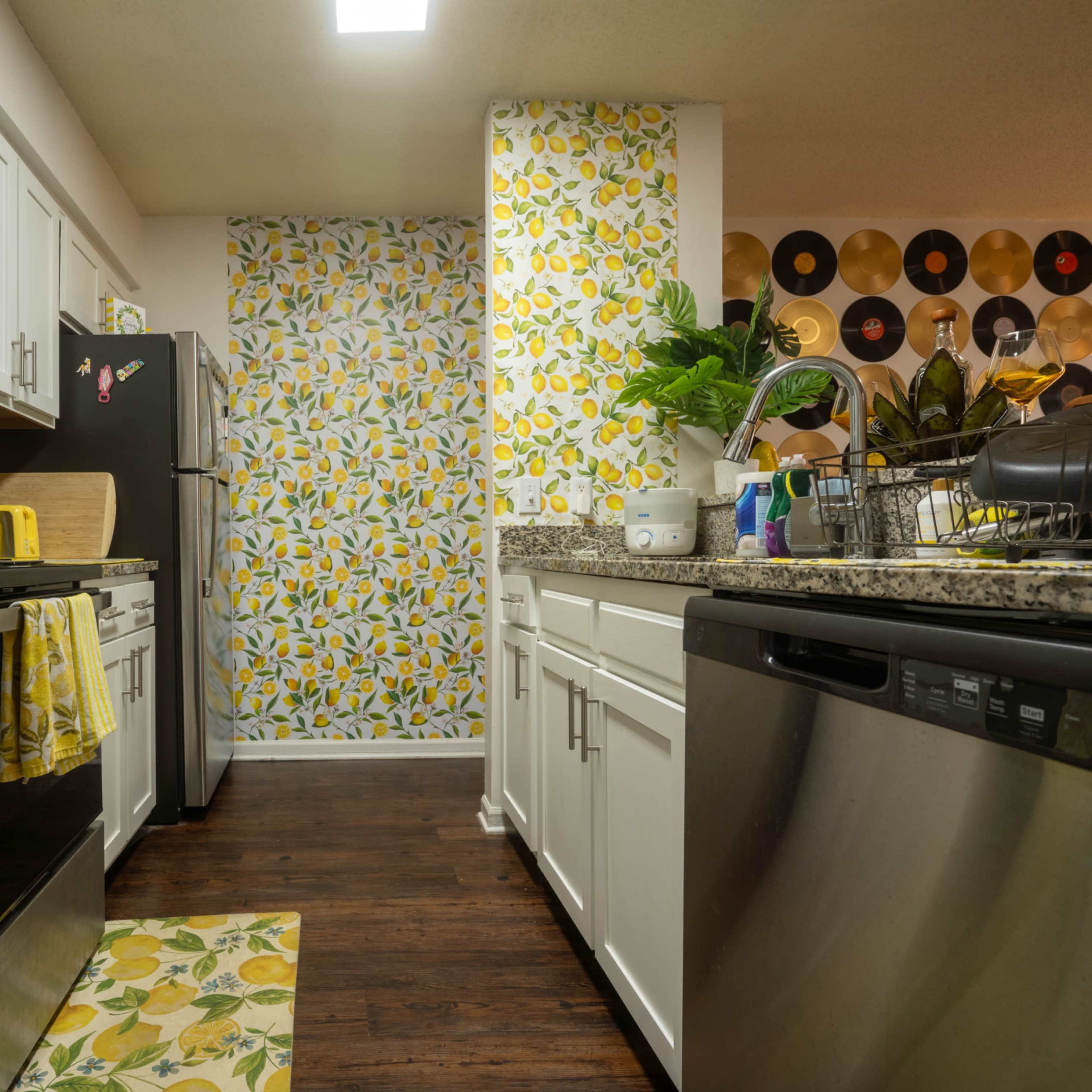 The kitchen features white cabinets, a black refrigerator, granite countertops, and lemon-themed decor on the walls and dish towels.