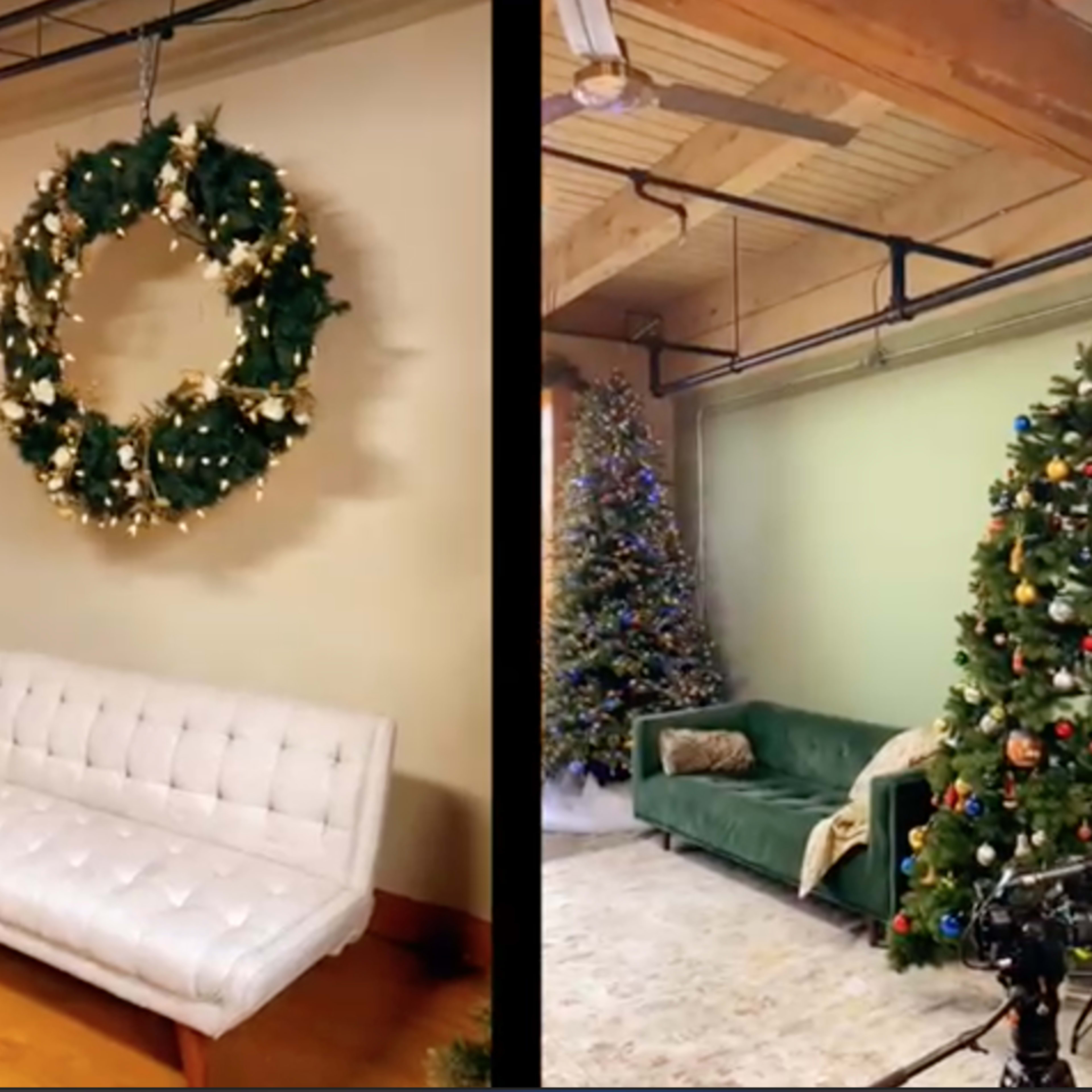 A decorated living space with a large wreath on the wall and two Christmas trees, one on each side, beside a white couch.