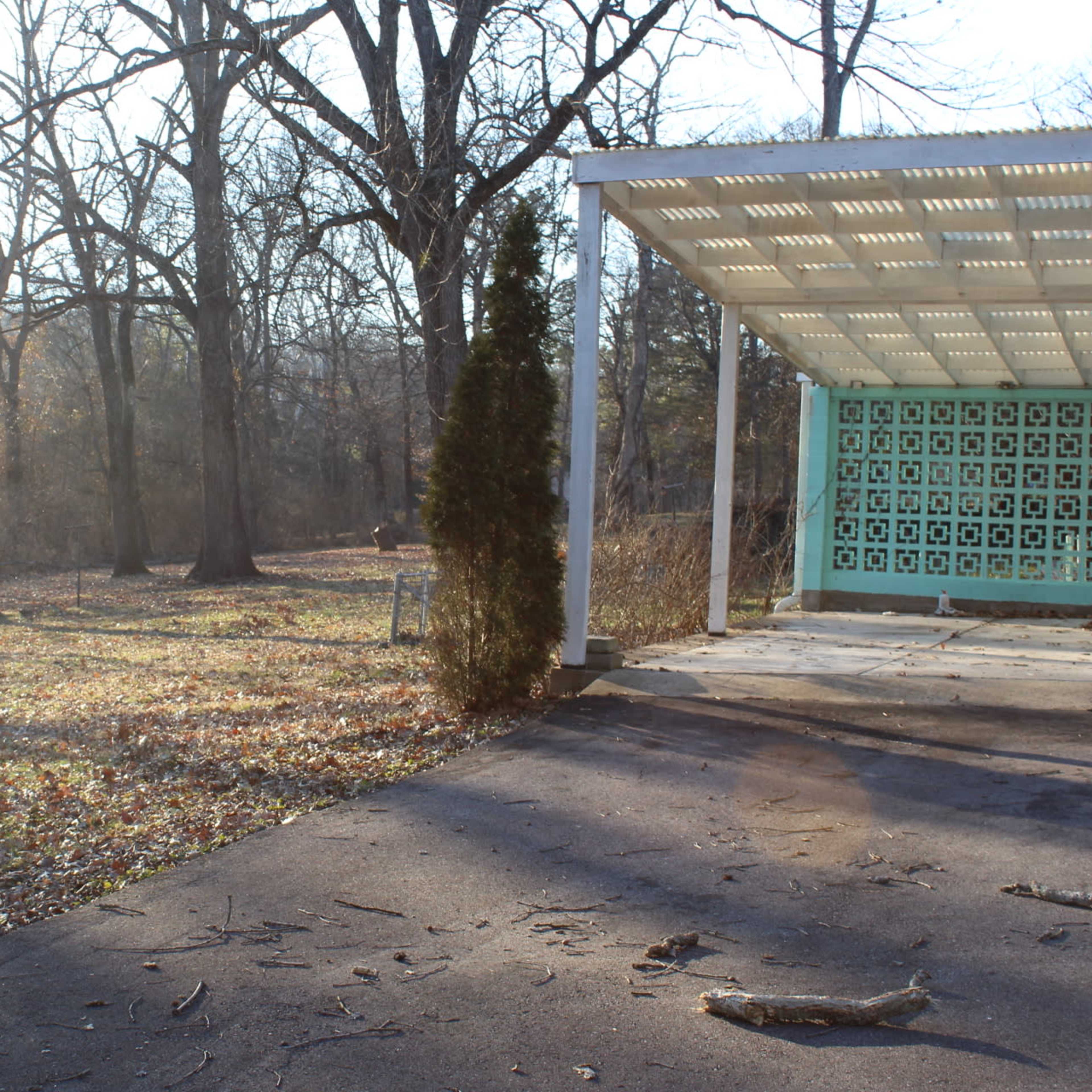 A paved area with a patterned wall is surrounded by a clearing and trees in a natural setting.