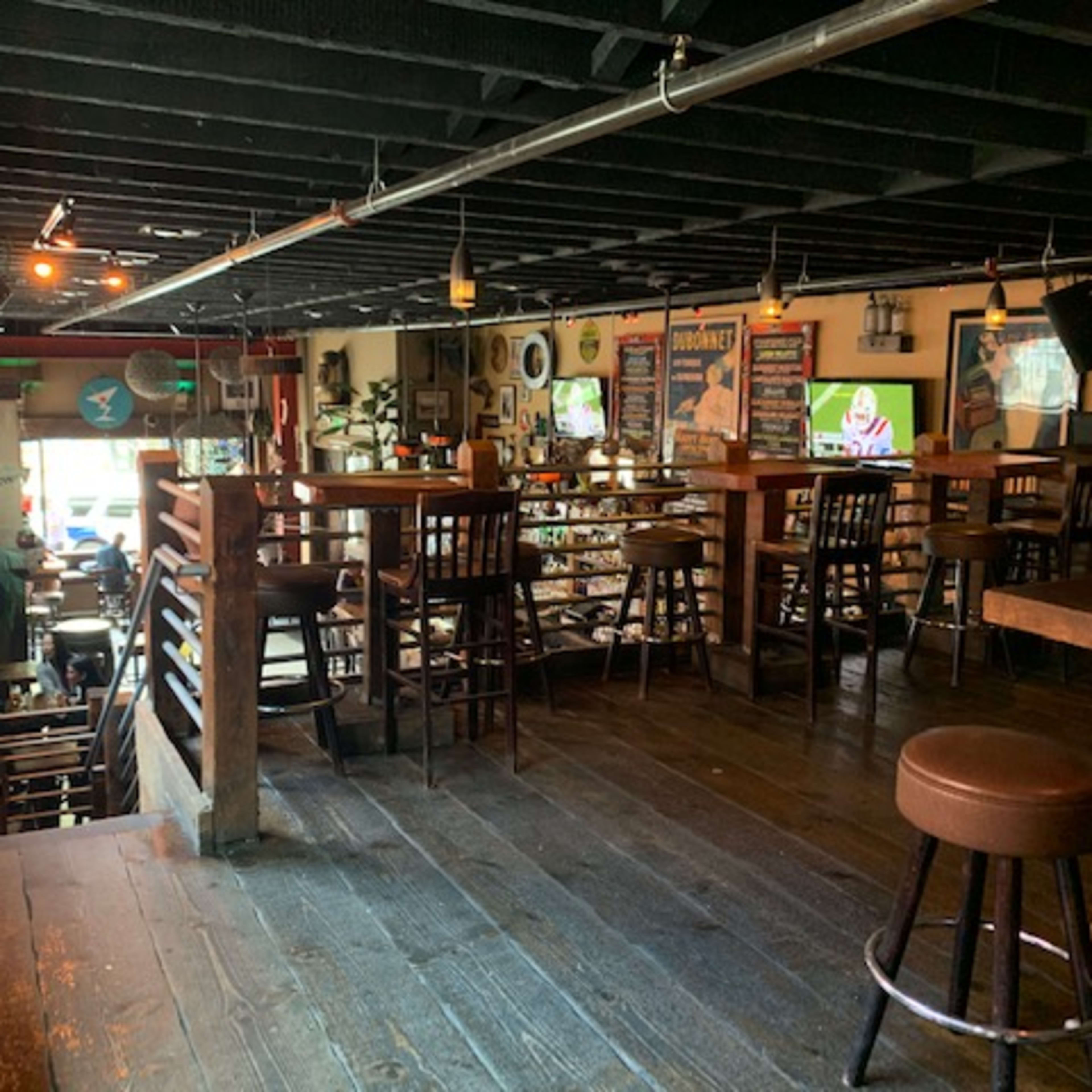 A rustic bar area with wooden furniture, including tables and stools, illuminated by warm lighting and featuring a variety of decorations on the walls.