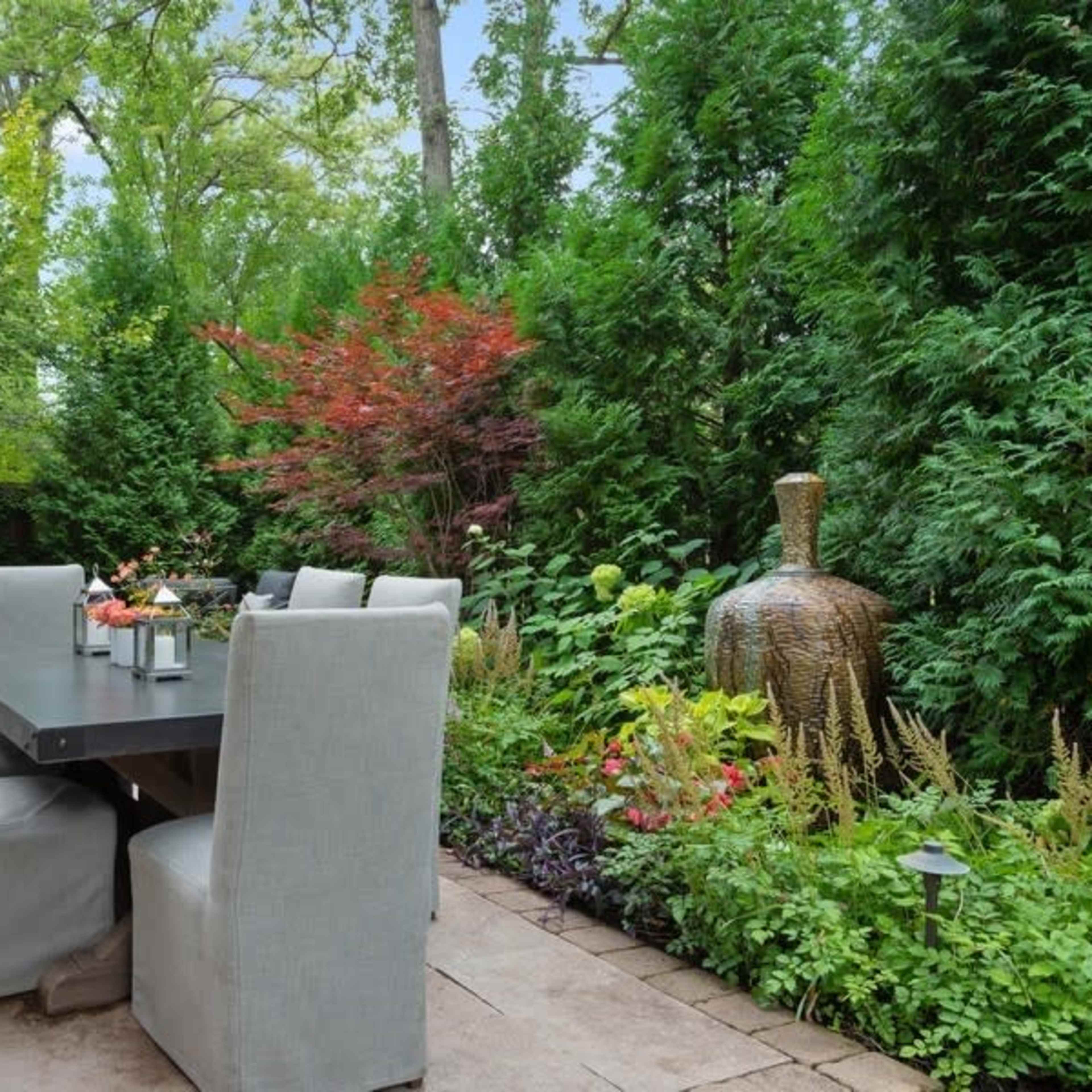 A patio area featuring a dining table with upholstered chairs surrounded by various plants and decorative elements.