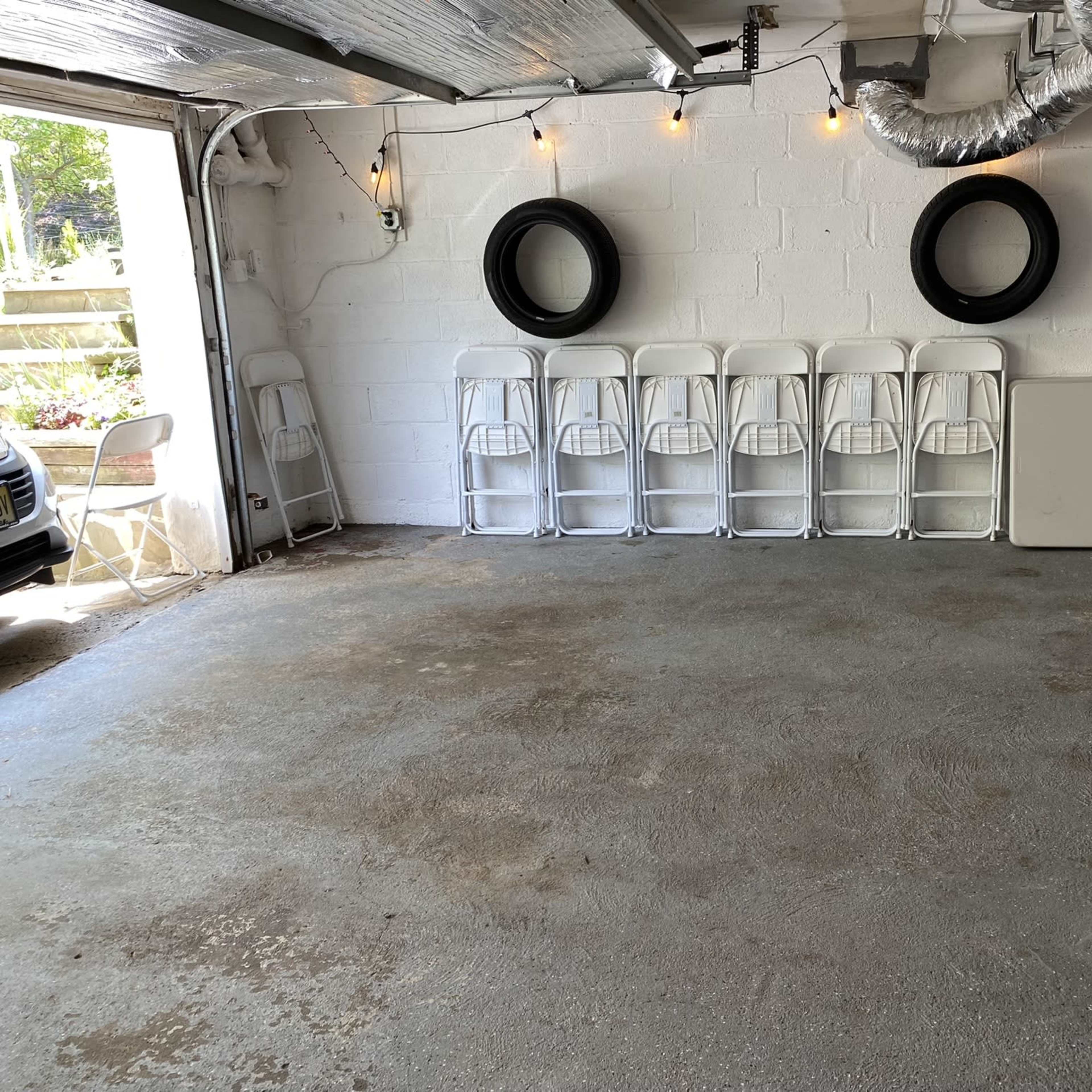 A garage with a clean concrete floor, several white folding chairs lined up against a wall, and two tires mounted on the wall above the chairs.