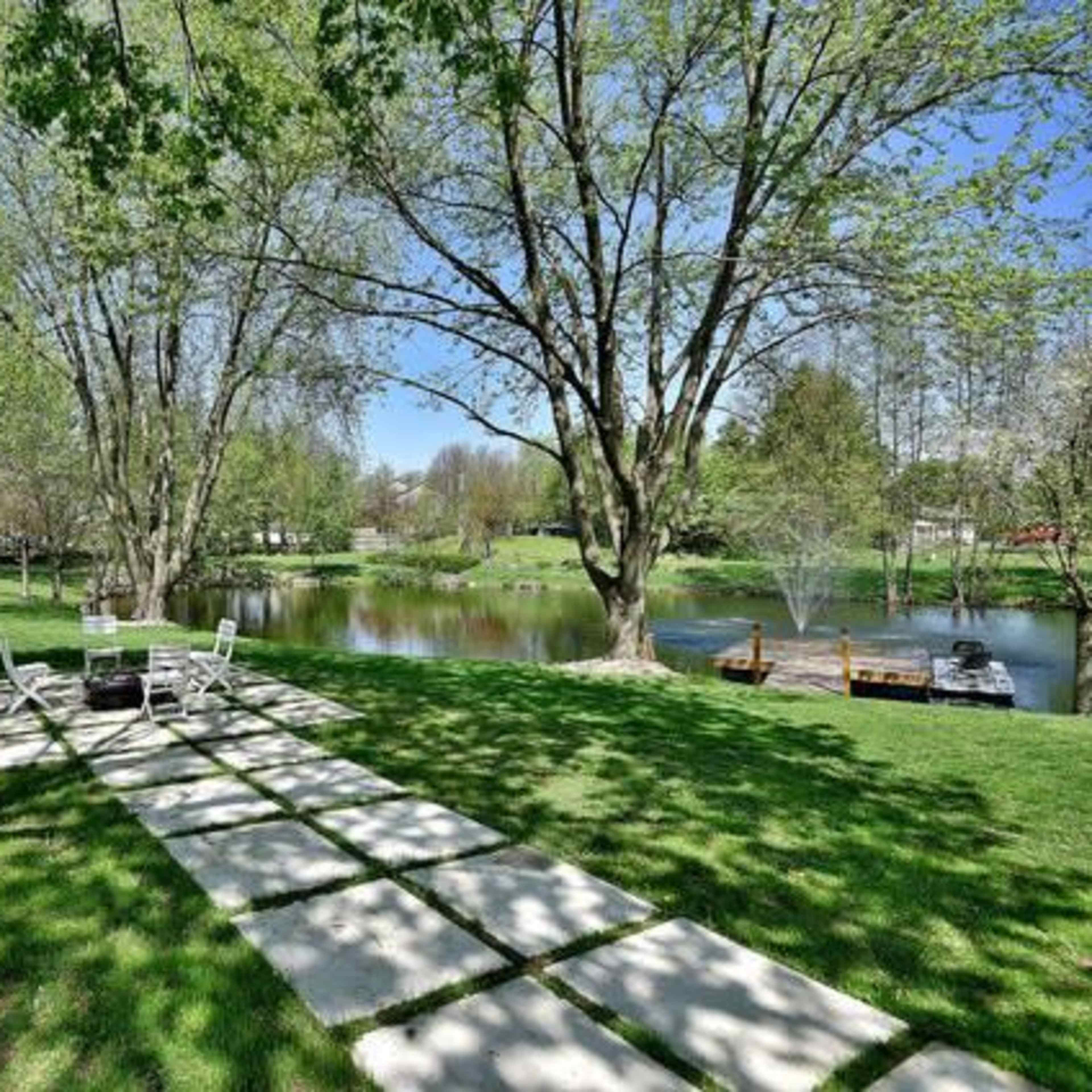 A grassy area with a stone pathway leading to a pond surrounded by trees.