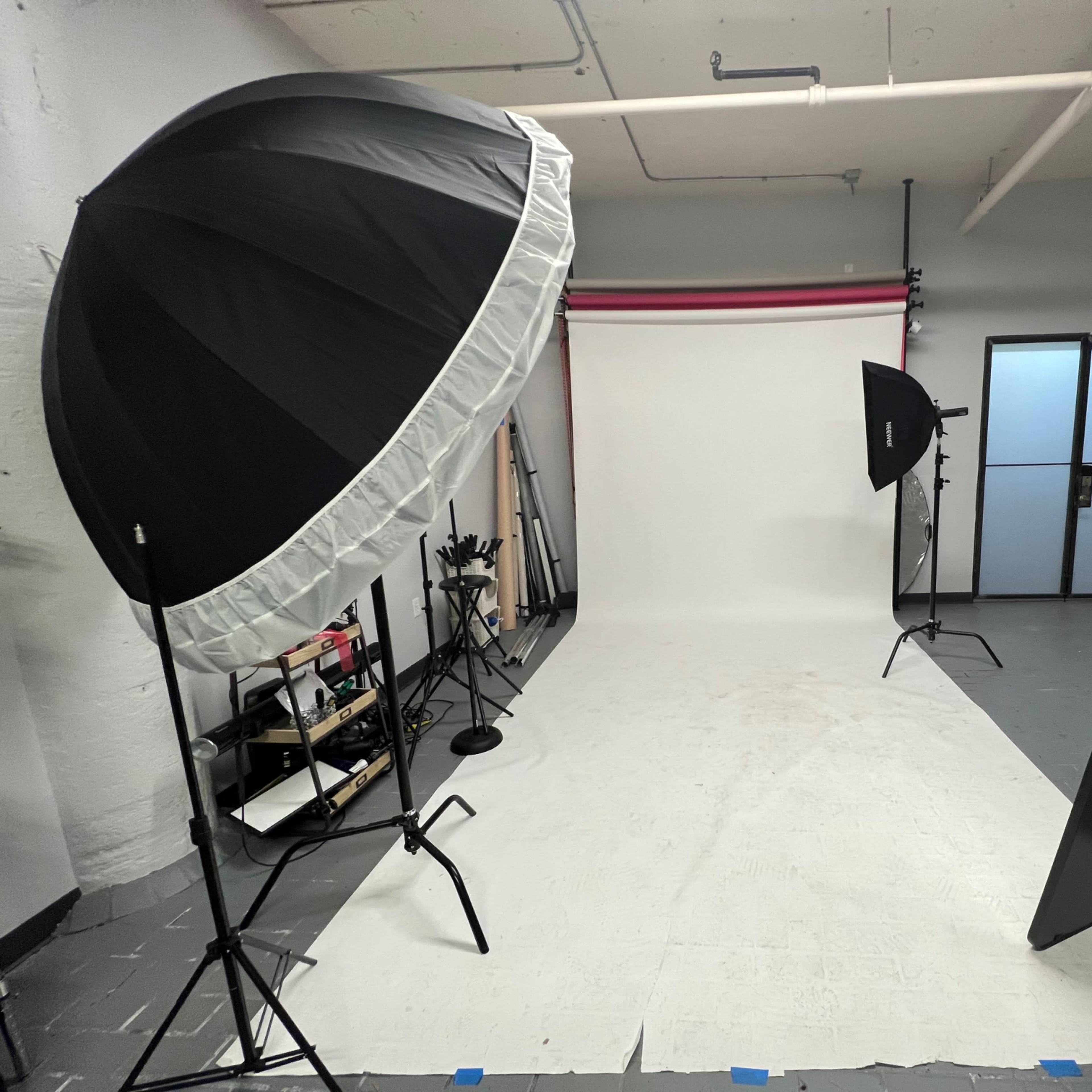 A photography studio with two light umbrellas, a large mirror, and a blank backdrop.