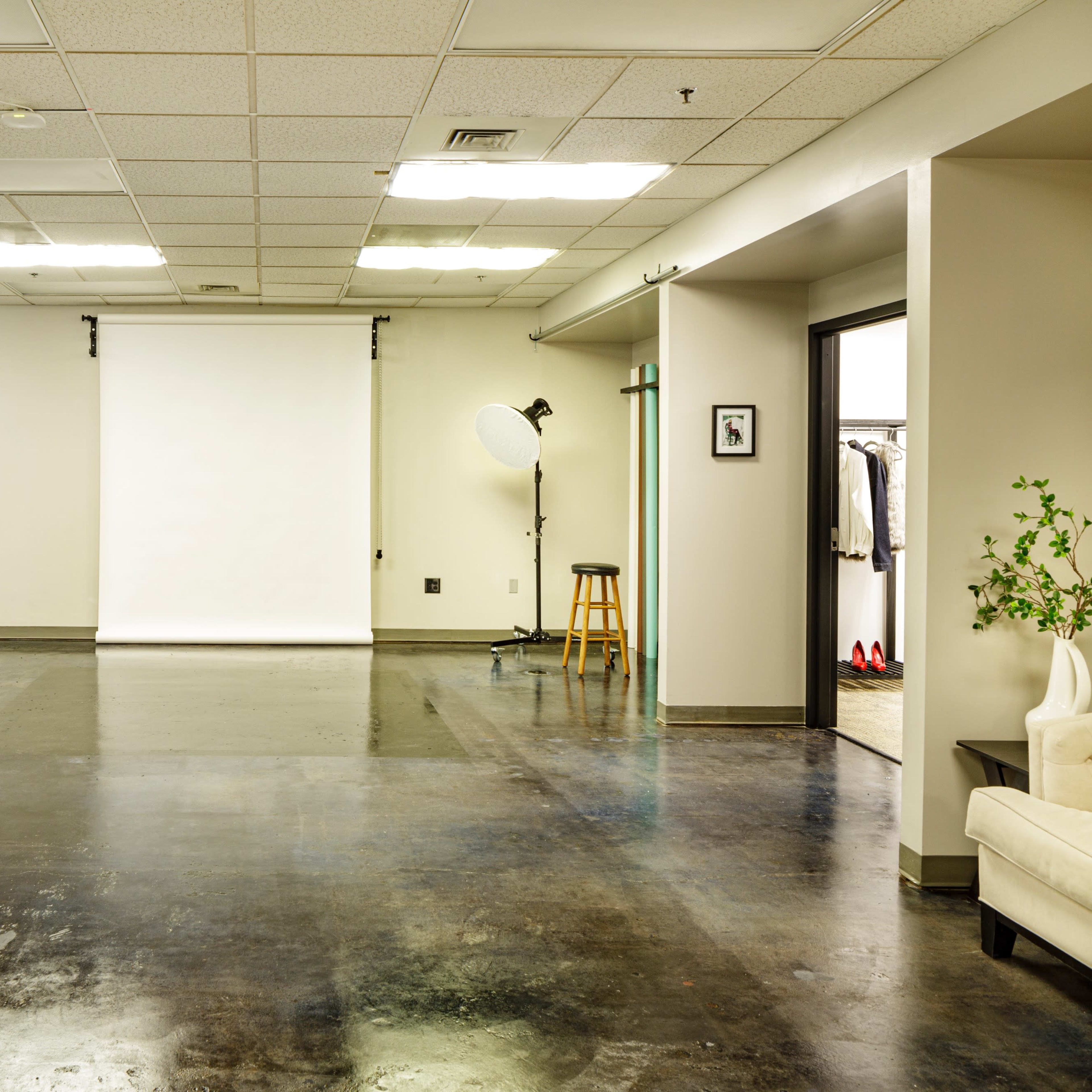 A spacious studio with two large softbox lights, a backdrop, and a seating area.