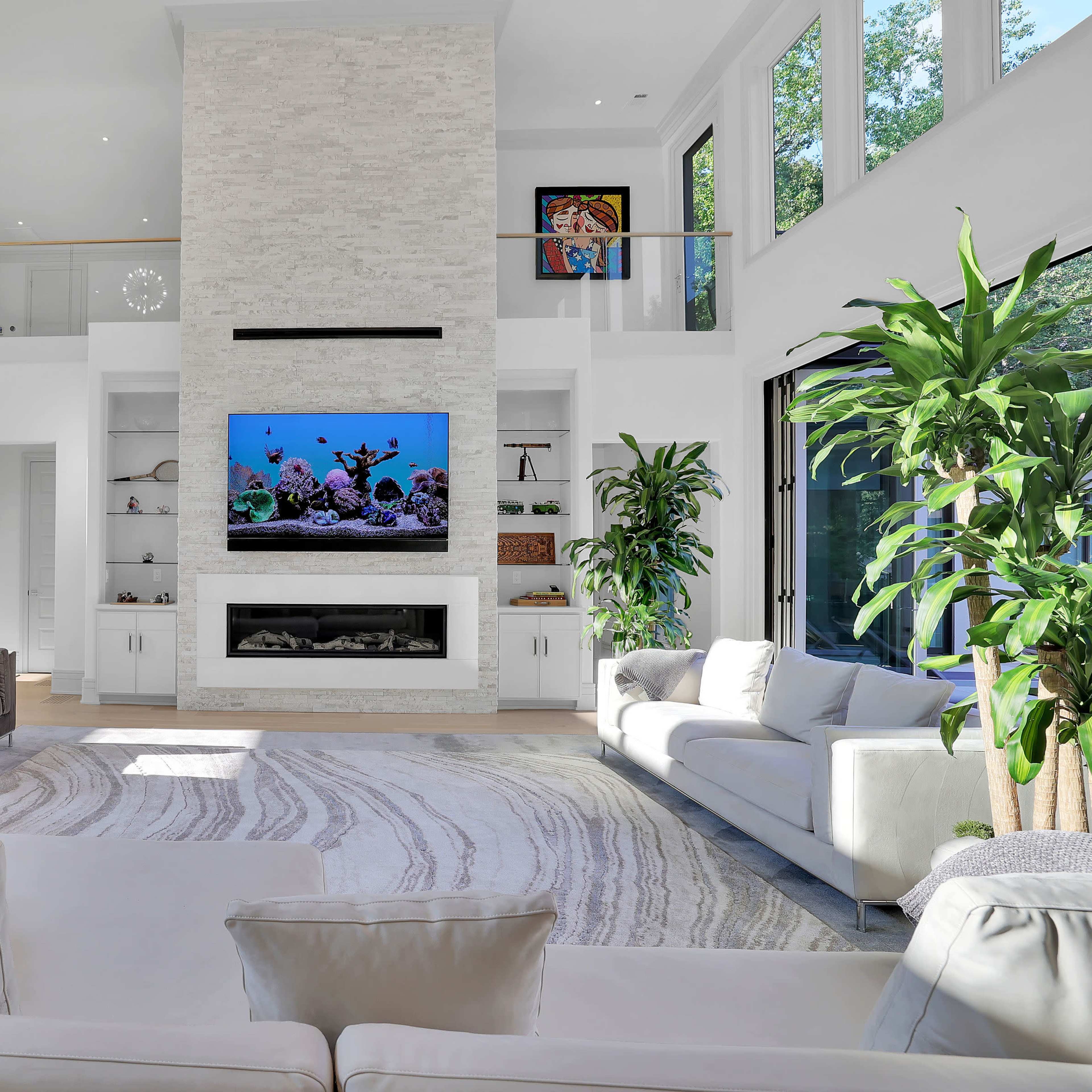 The spacious living room features a large television mounted above a modern fireplace, surrounded by contemporary furniture and large windows that allow natural light to fill the space.