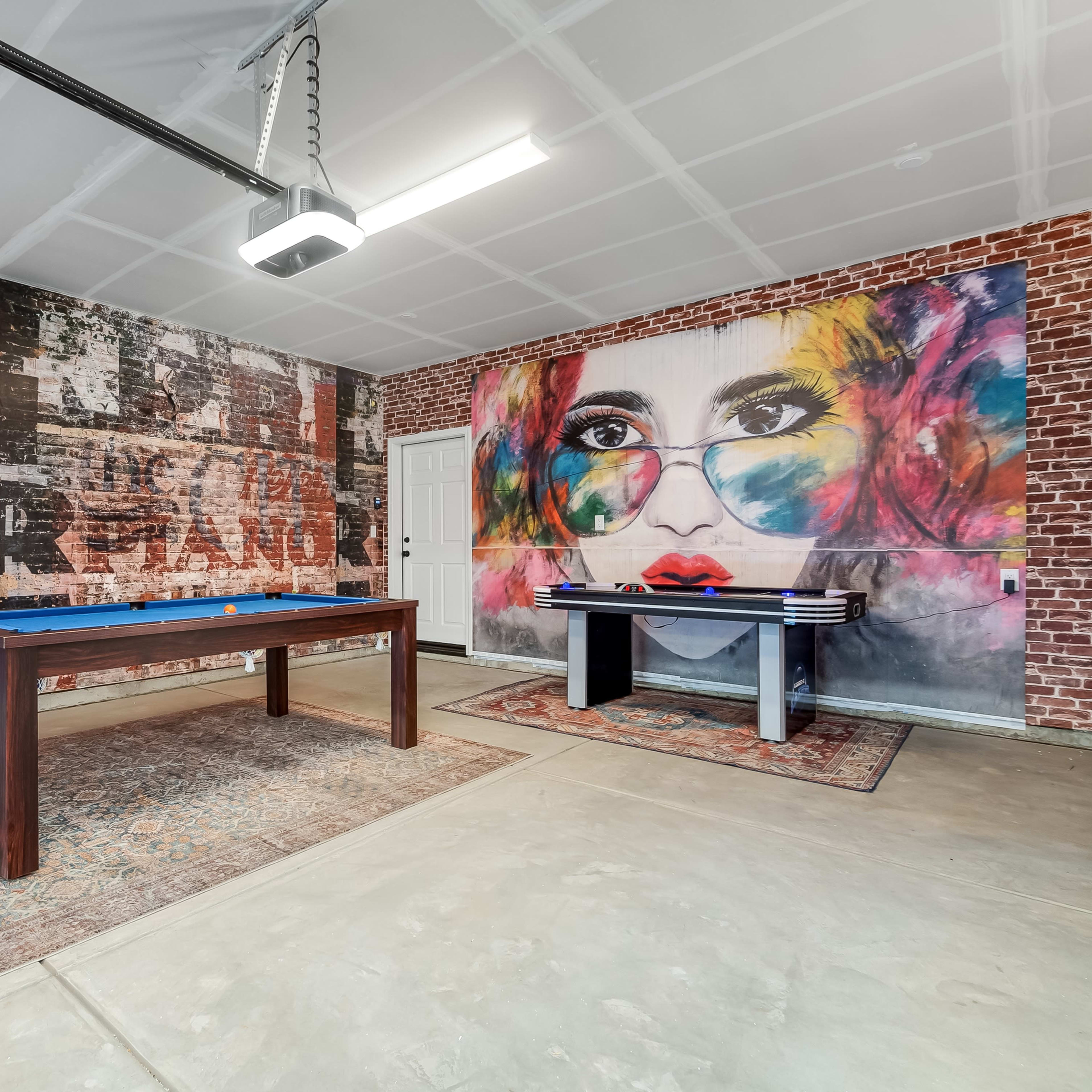 A garage with a pool table and a vibrant mural of a woman's face on a brick wall.