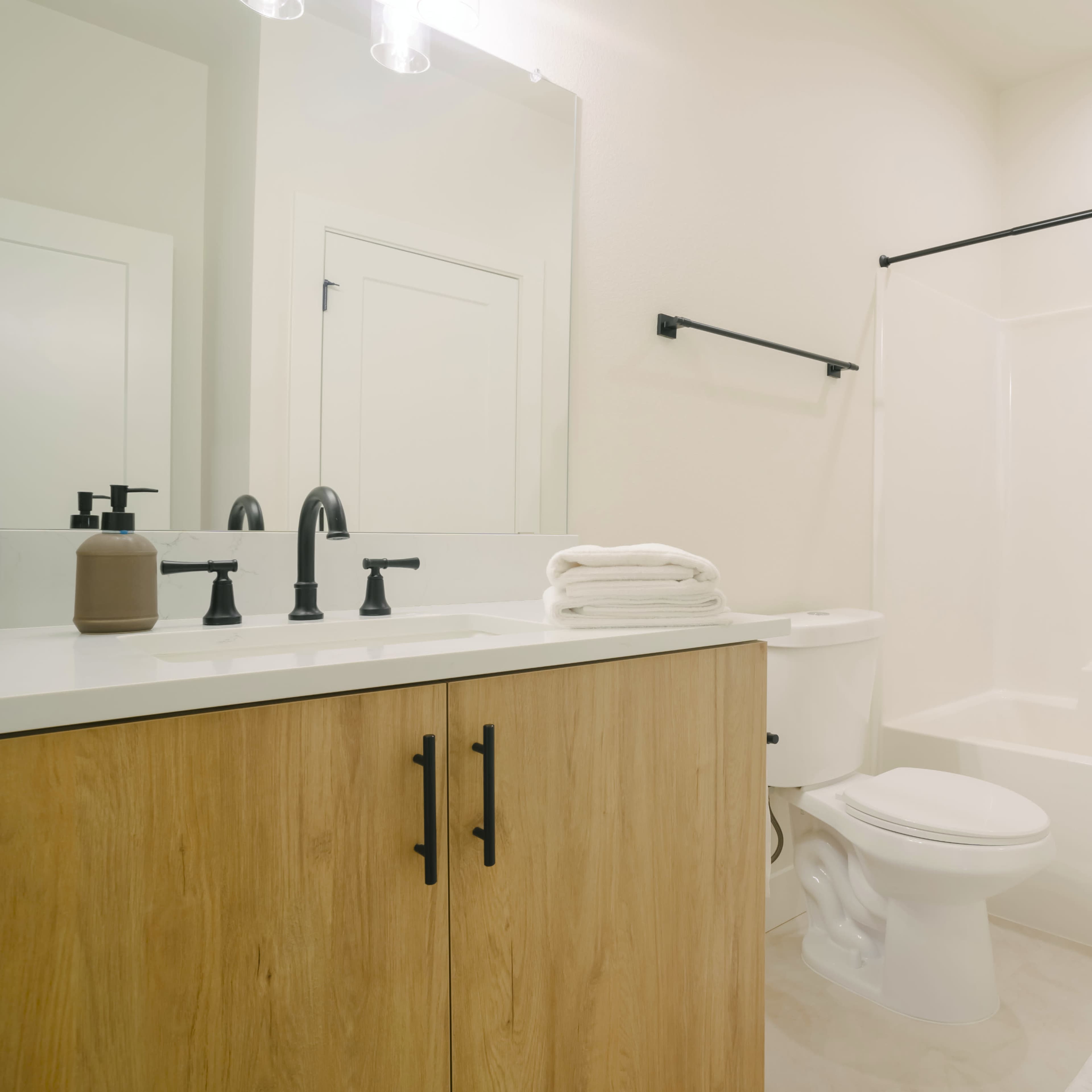 A clean bathroom features a sink with a wooden cabinet, a toilet, and a bathtub with a shower curtain.