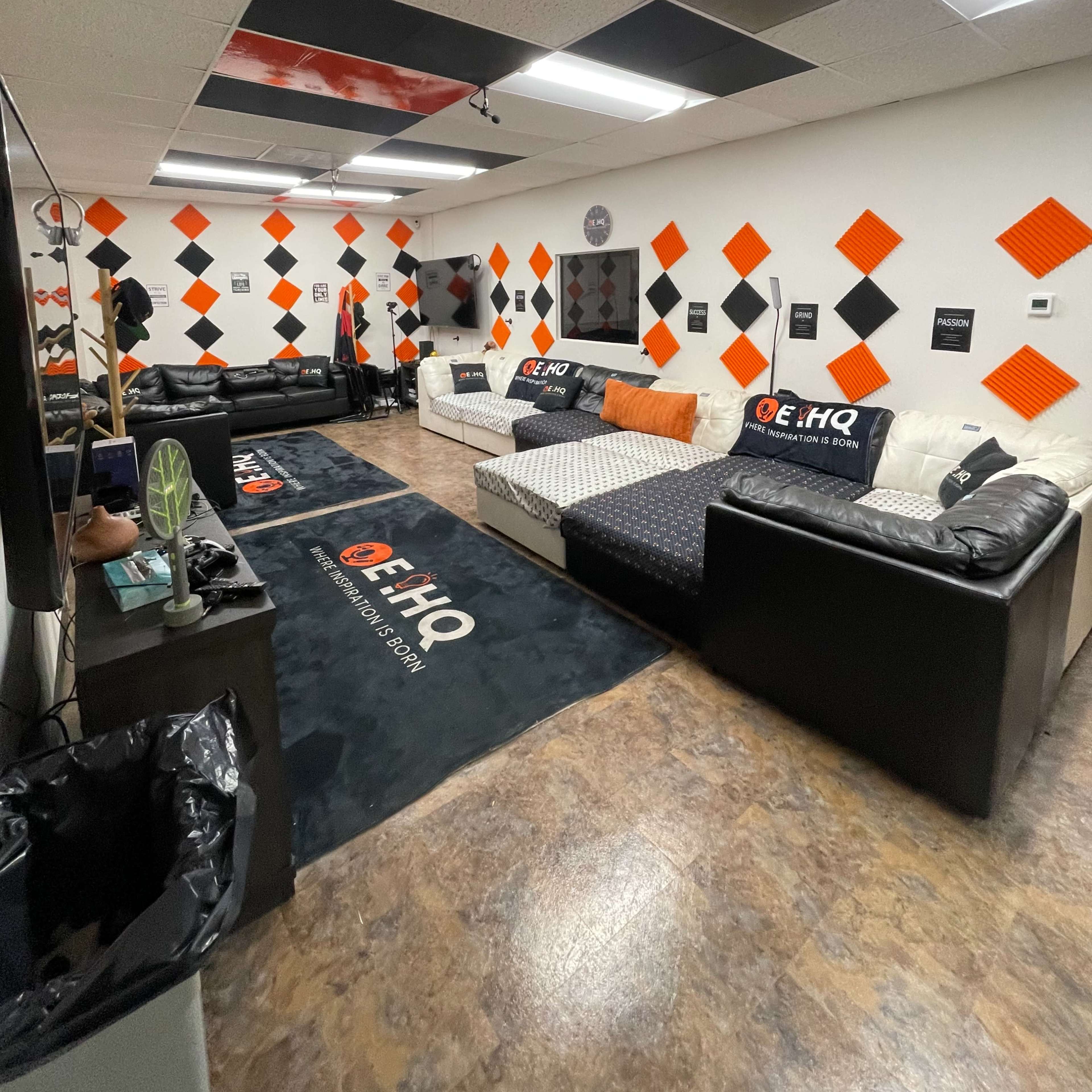 A lounge area with black and orange decor, featuring two couches, walls adorned with diamond-shaped designs, and a carpet branded with "E HQ."