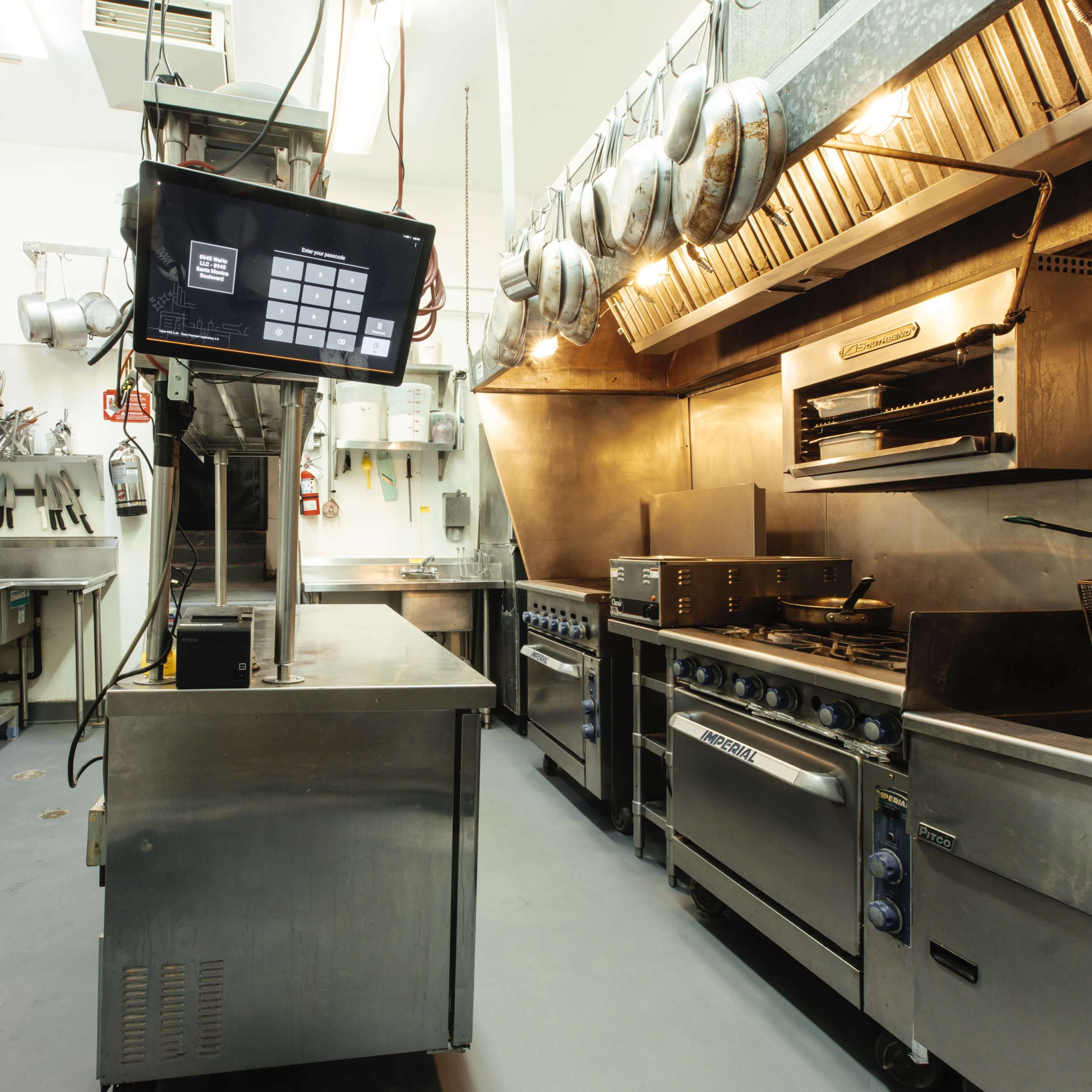 A commercial kitchen equipped with stainless steel appliances, countertops, and hanging pots.