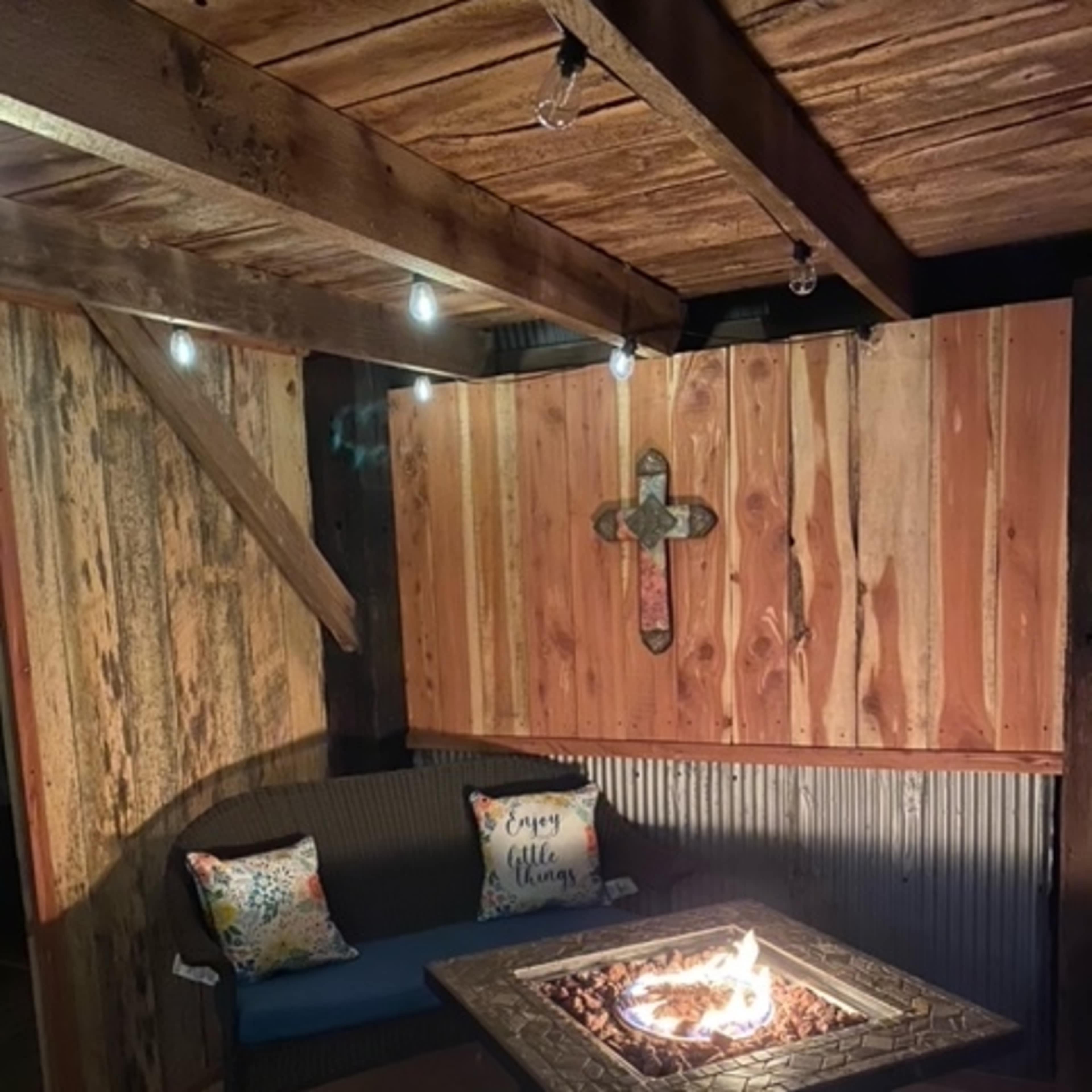 A cozy outdoor seating area featuring a fire pit surrounded by wooden walls and accent lighting.