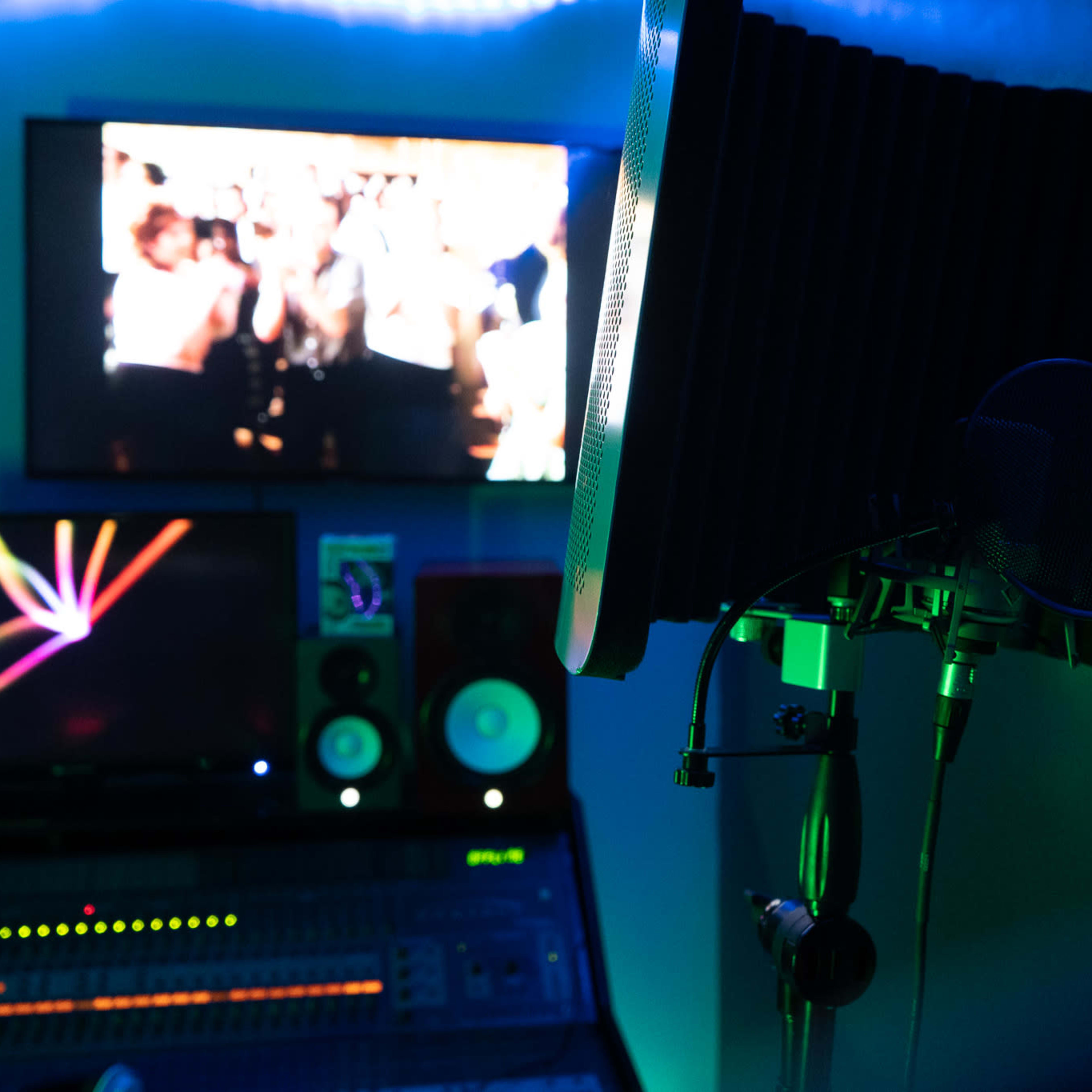 A recording studio is shown, featuring a microphone and pop filter in front of multiple computer screens and speakers.