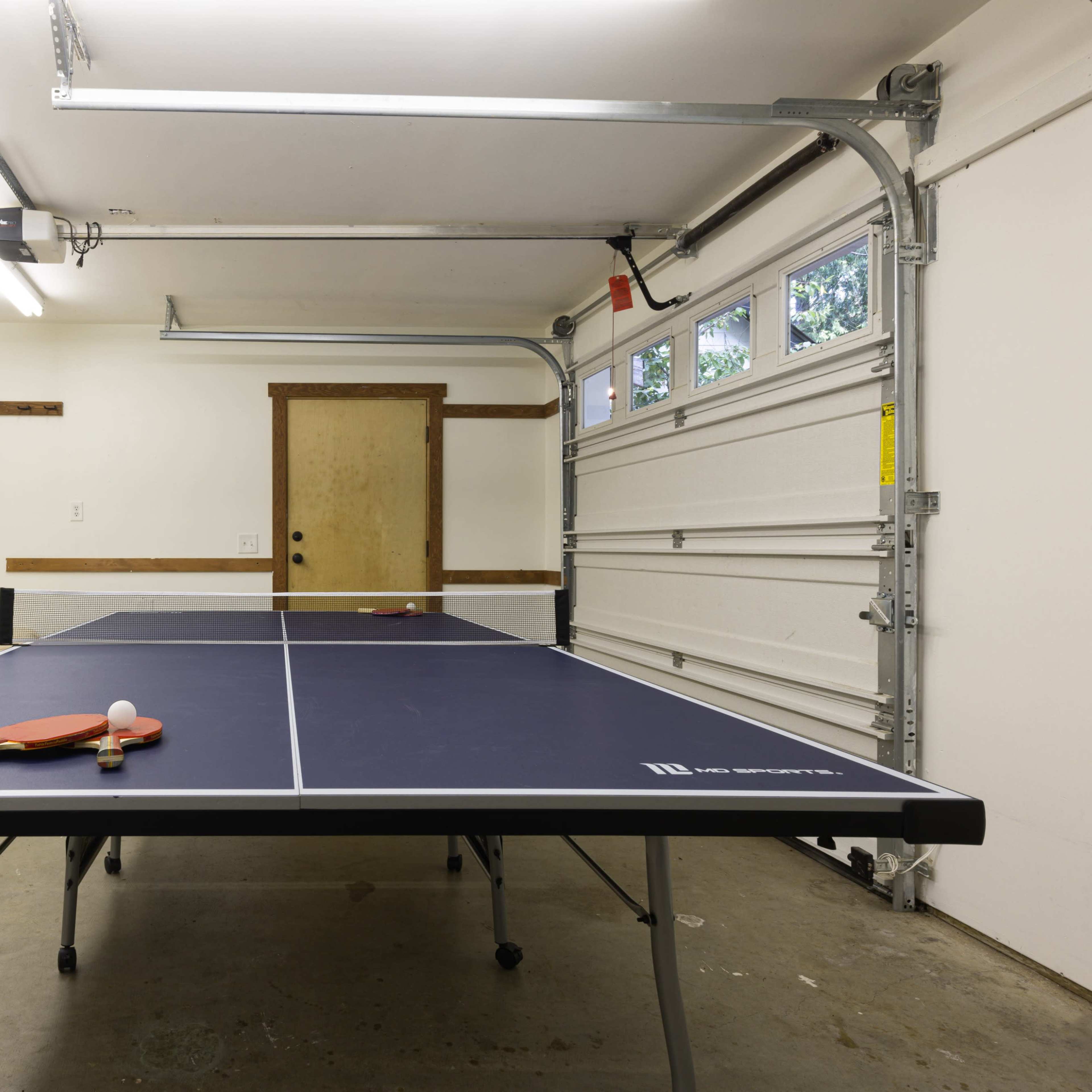 A ping pong table is set up in a garage next to a couch and a closed door.