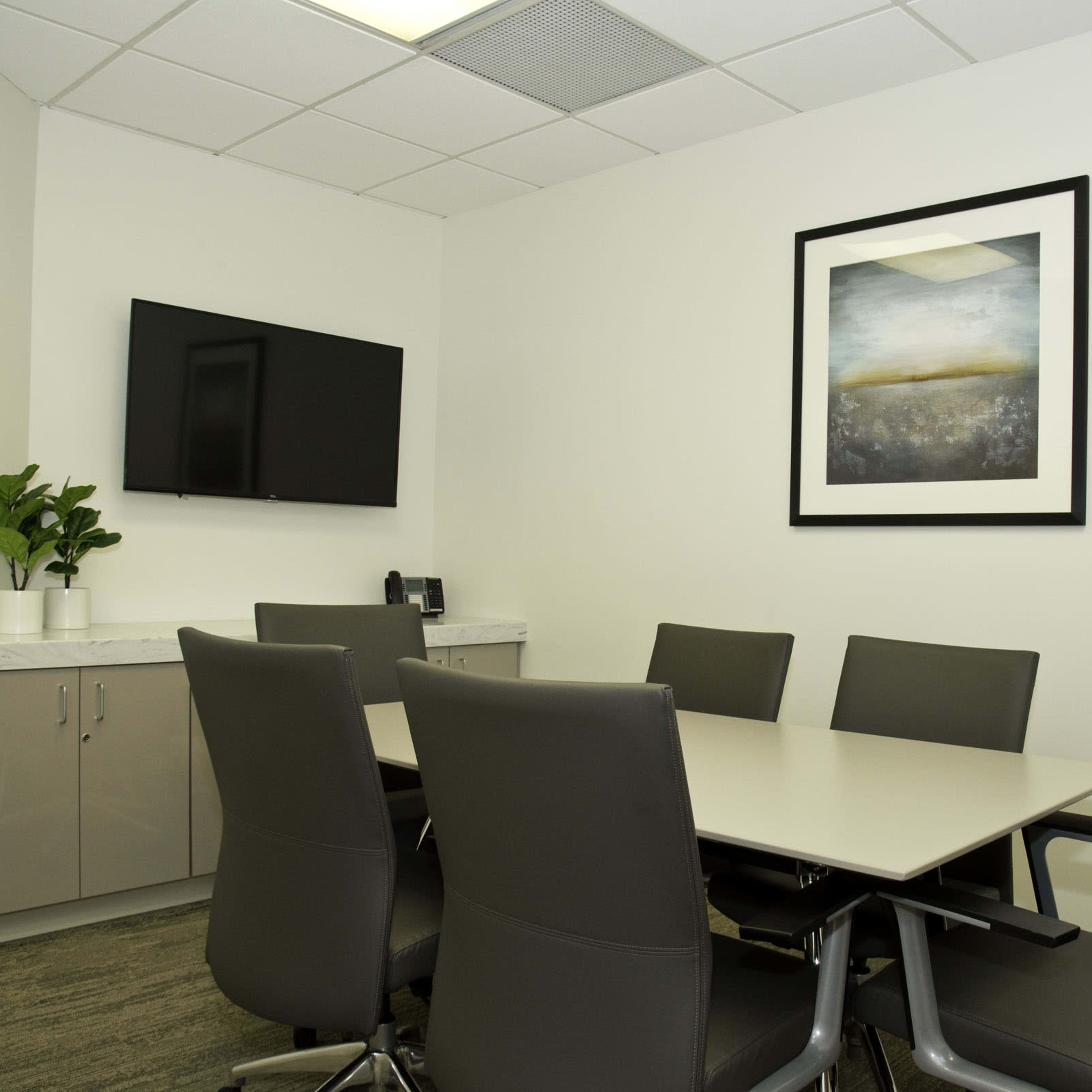 A conference room with a large table surrounded by eight chairs, a mounted television, and a piece of wall art.