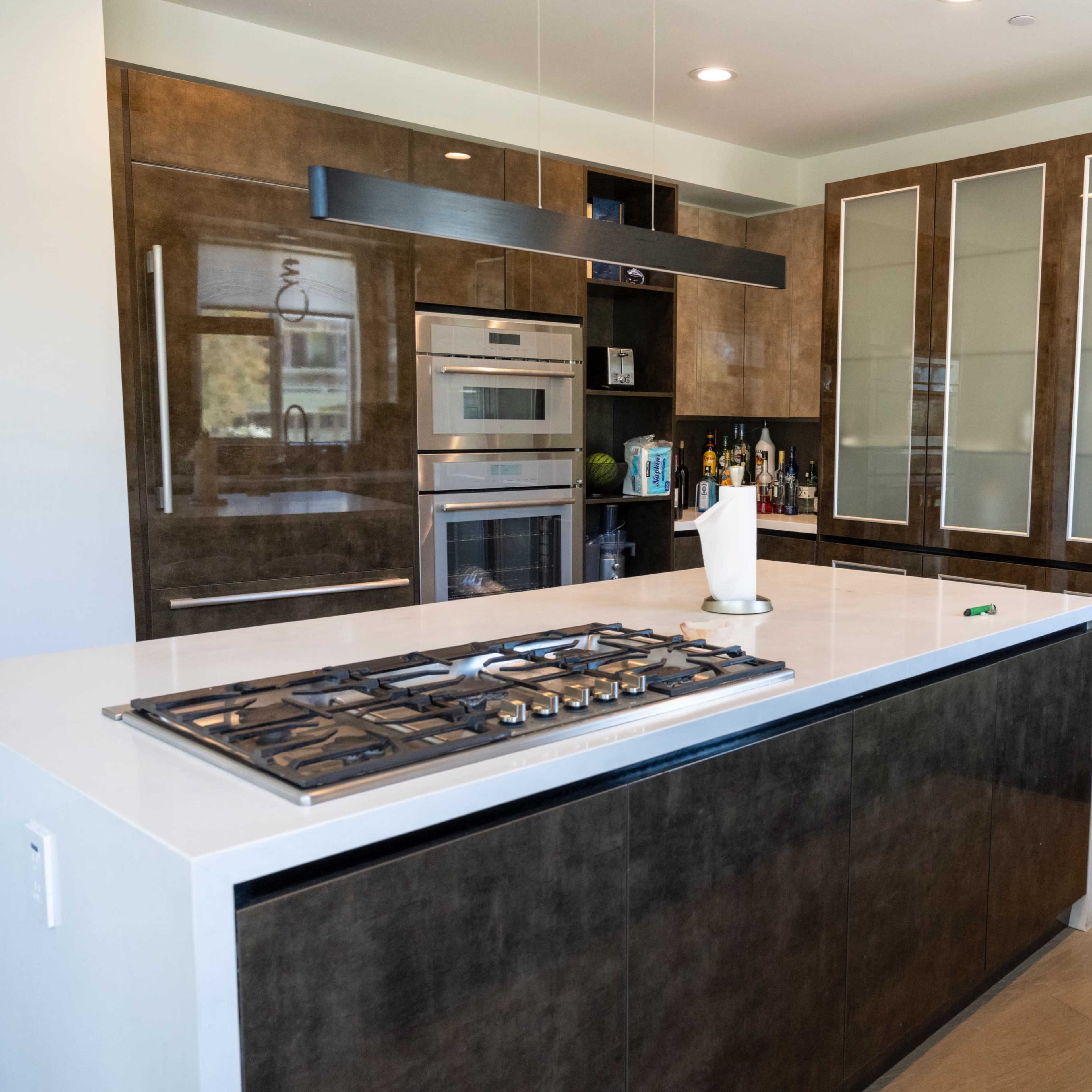 A modern kitchen featuring a central island with a gas cooktop, sleek cabinetry, and built-in appliances.
