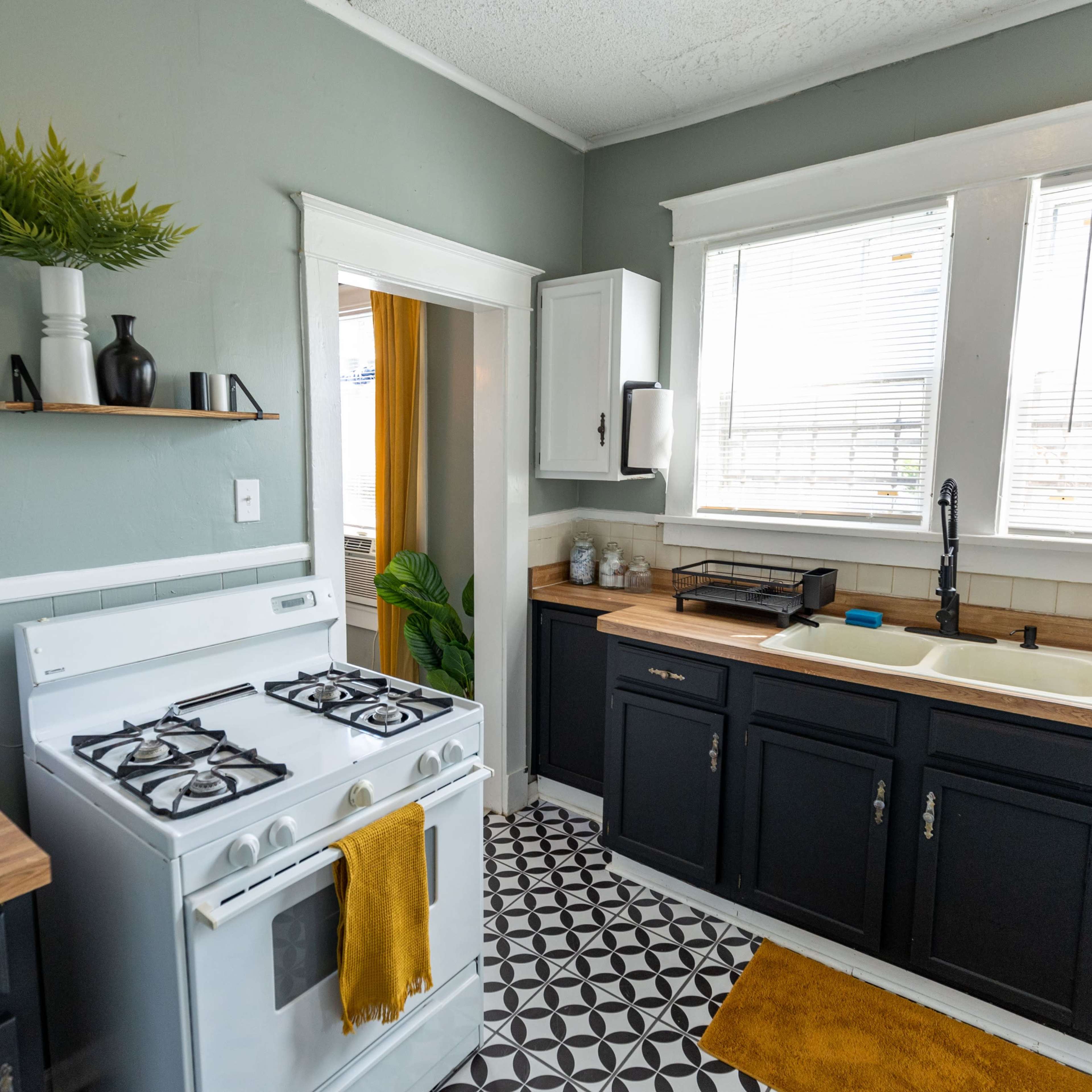 A modern kitchen features a white stove, black cabinets, a sink with a faucet, and patterned floor tiles.