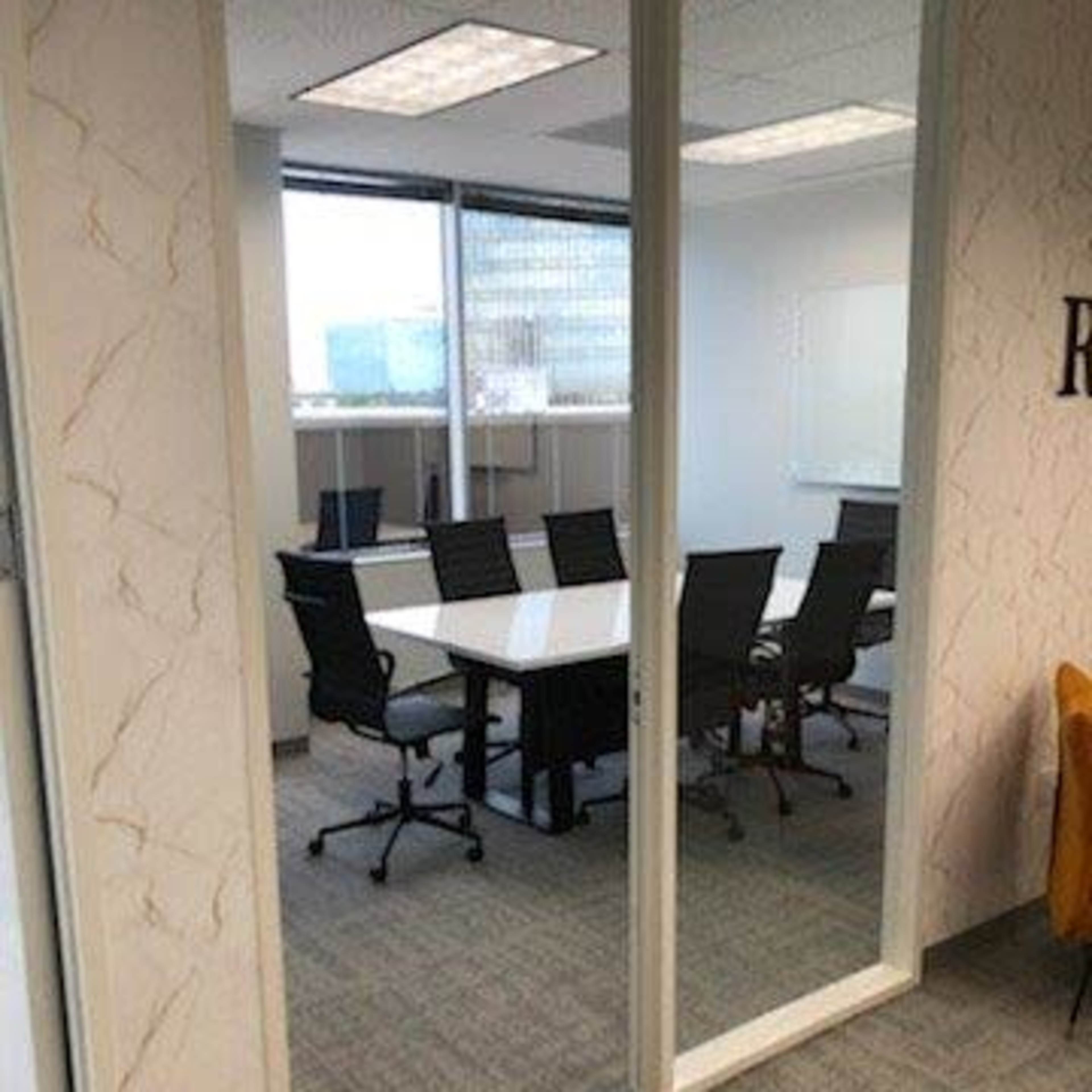 A conference room with a large table surrounded by office chairs, visible through glass walls.