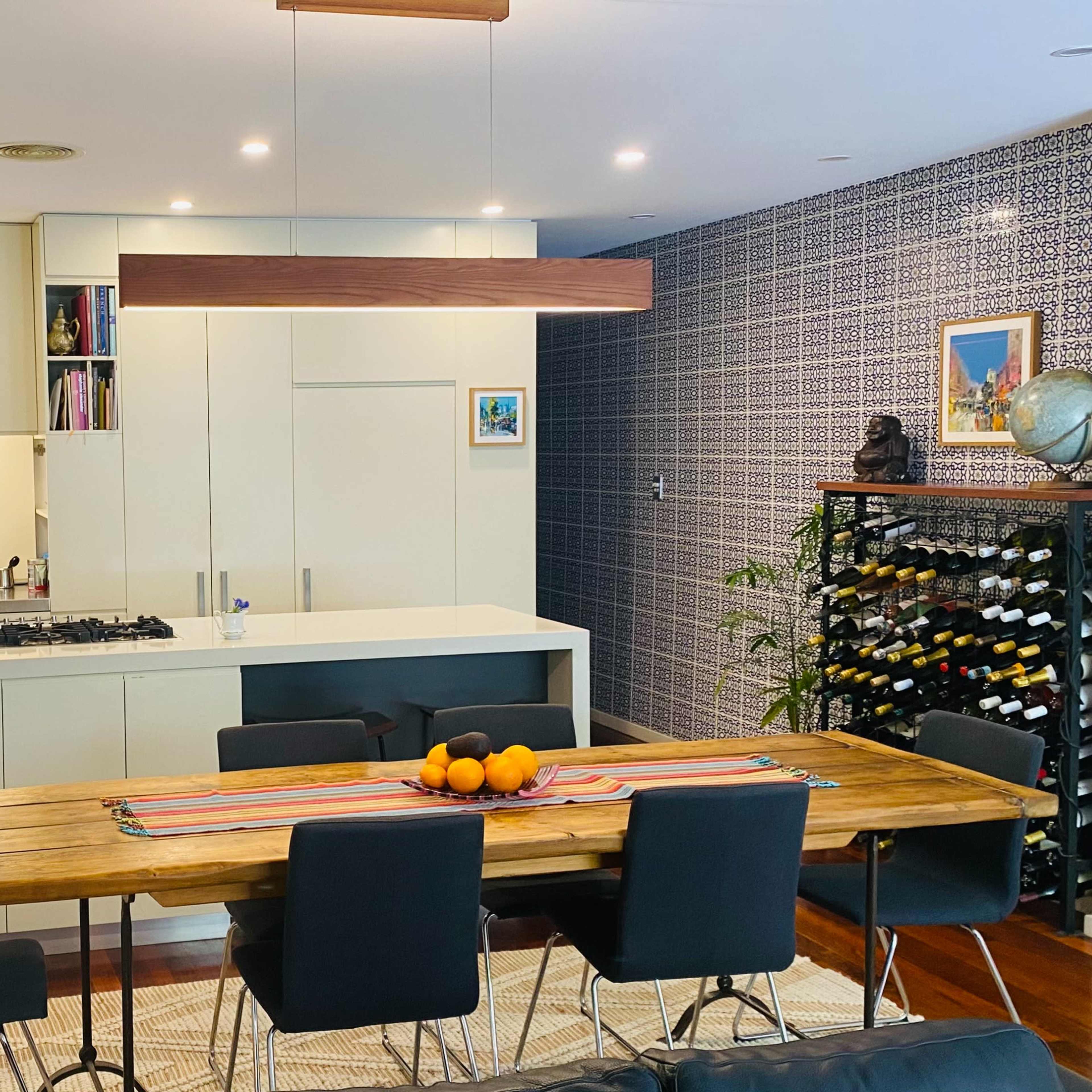 A modern kitchen and dining area featuring a wooden dining table, black chairs, and a wall adorned with wine storage and artwork.