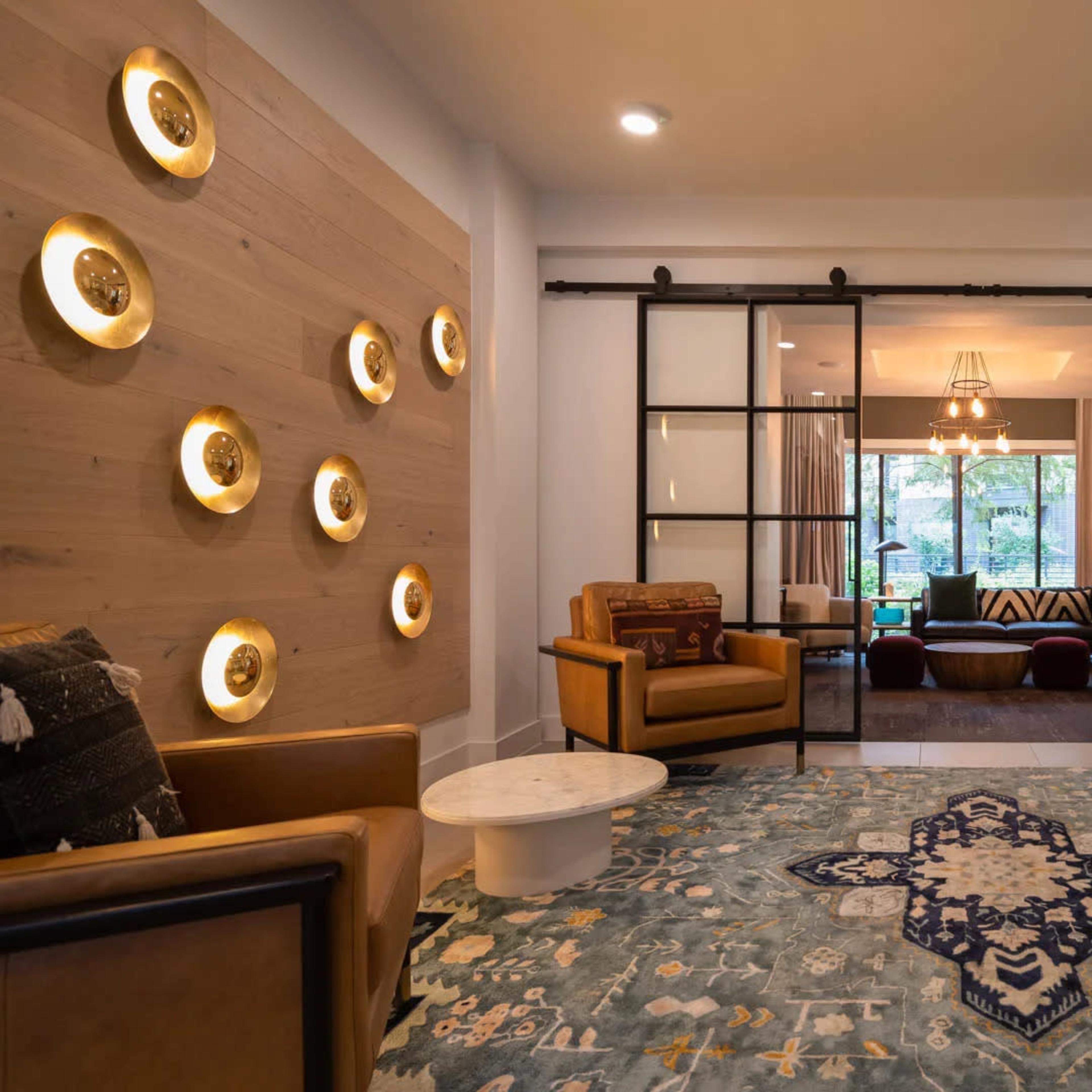 A modern lounge area features two leather chairs, a decorative rug, and sliding glass doors that lead to a brightly lit sitting room.