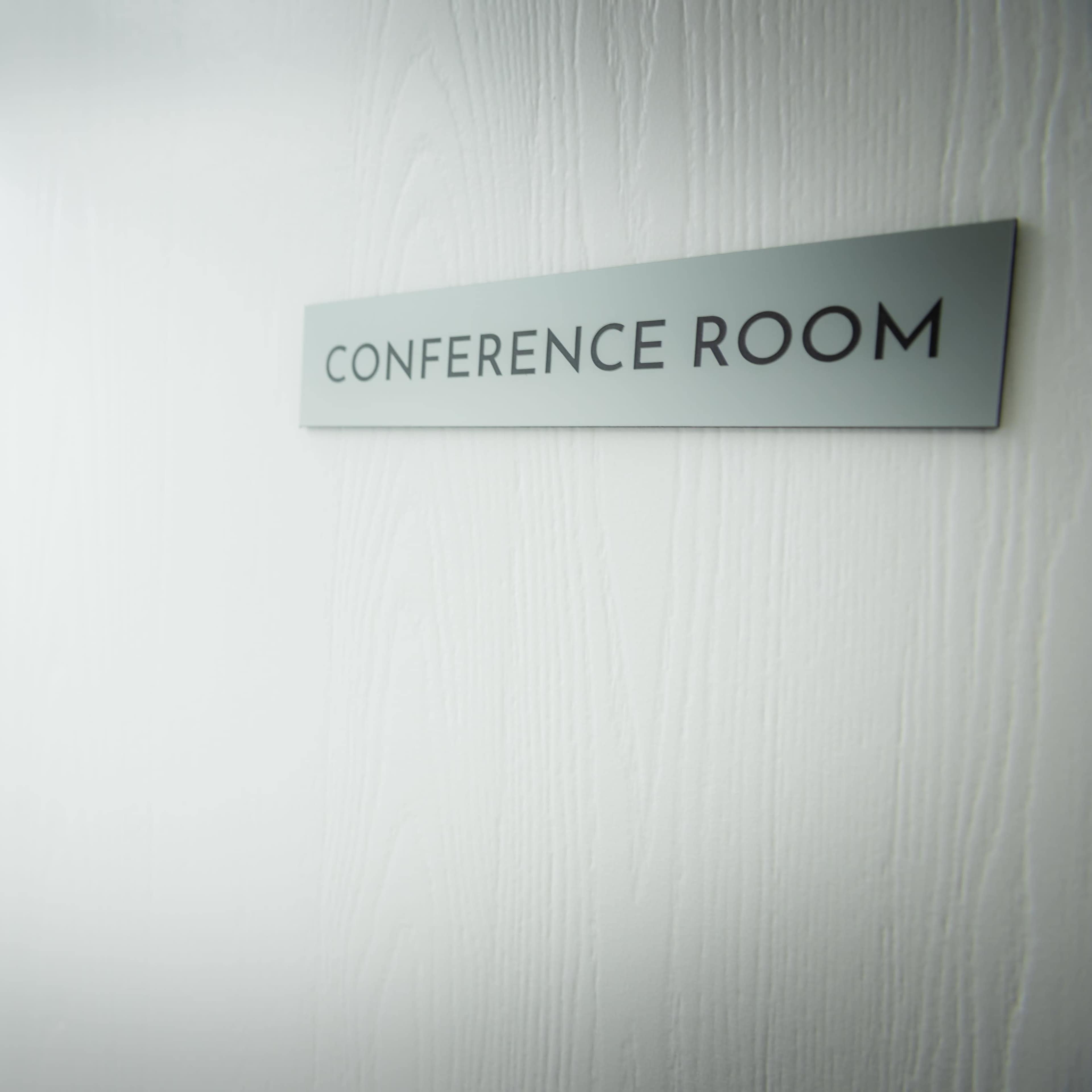 A sign labeled "CONFERENCE ROOM" is mounted on a white door, leading to a modern conference room with a large table and black chairs visible through the opening.