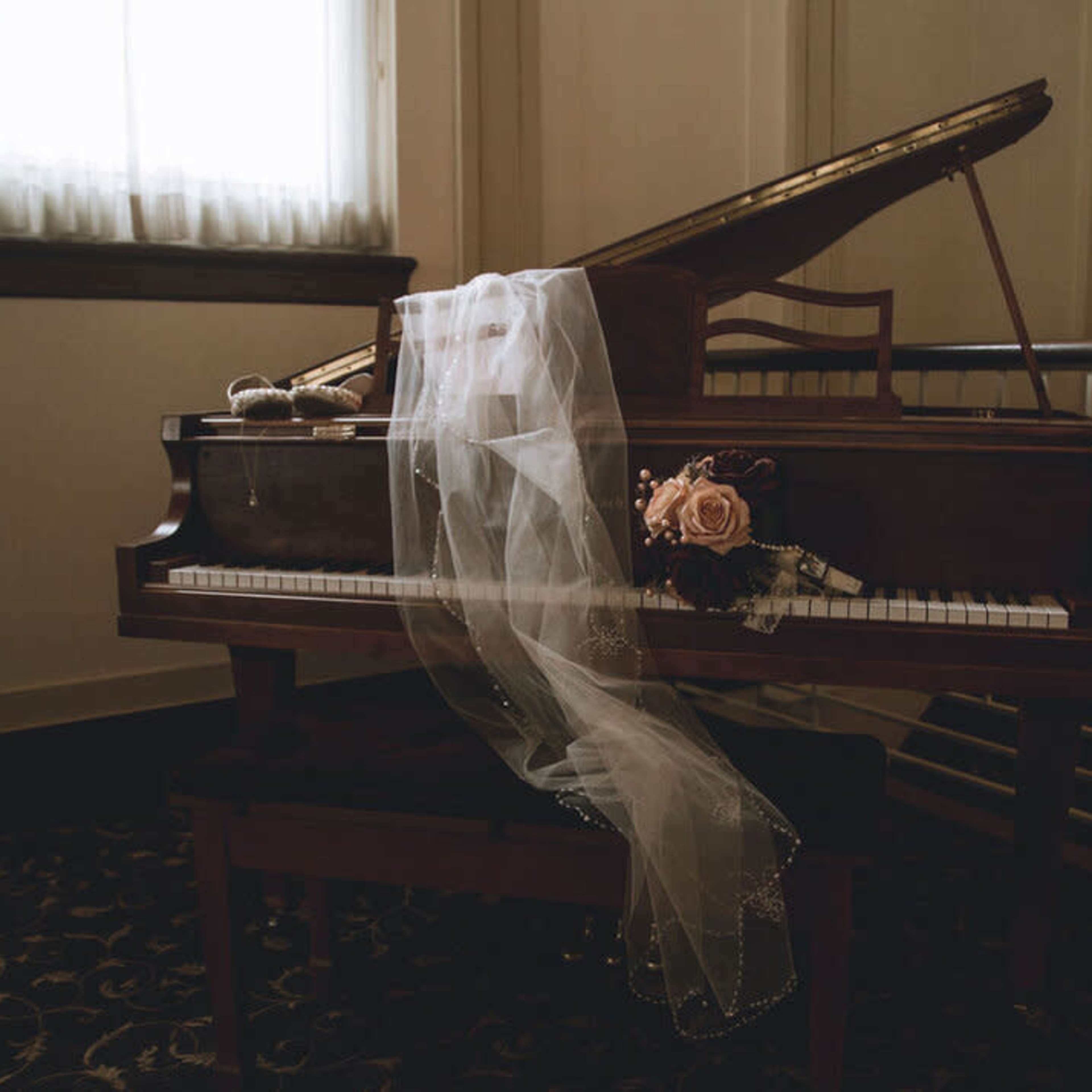 A grand piano adorned with a bouquet of flowers and a flowing veil sits in a softly lit room.