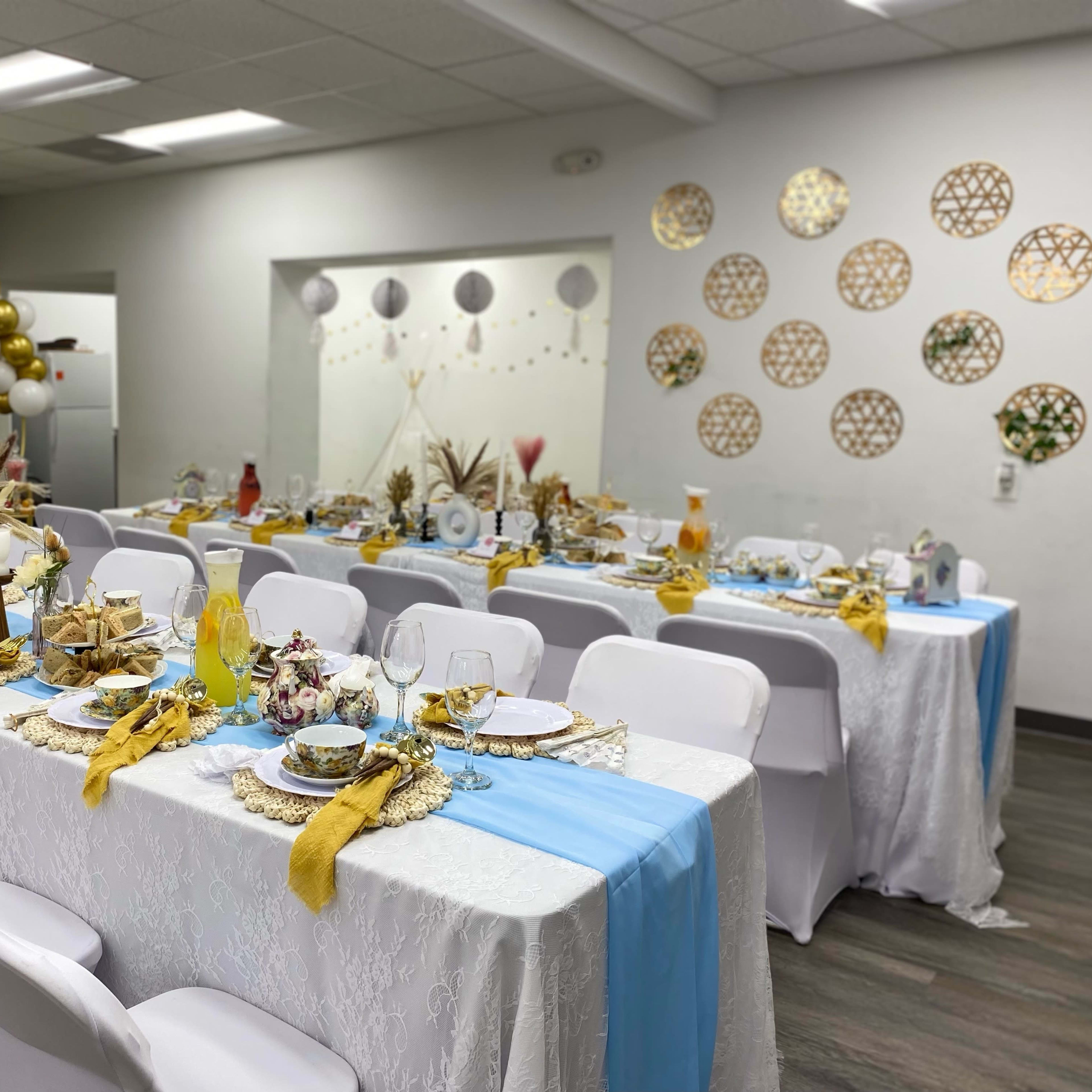 A decorated dining area with elegantly set tables adorned with white tablecloths, gold and blue accents, and decorative centerpieces for an event.