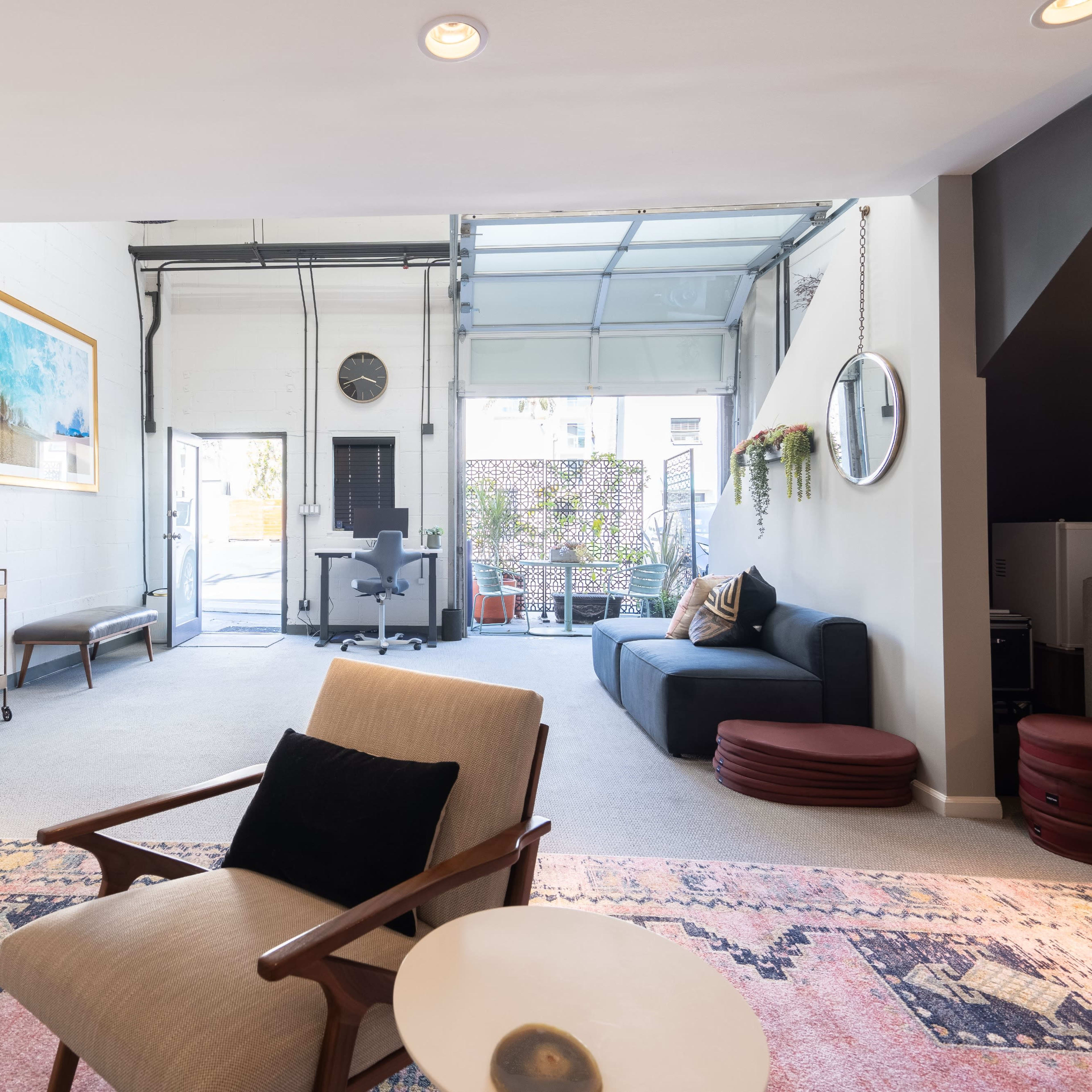 A spacious living area features modern furniture, a large wall art piece, and an open garage door leading to a patio.