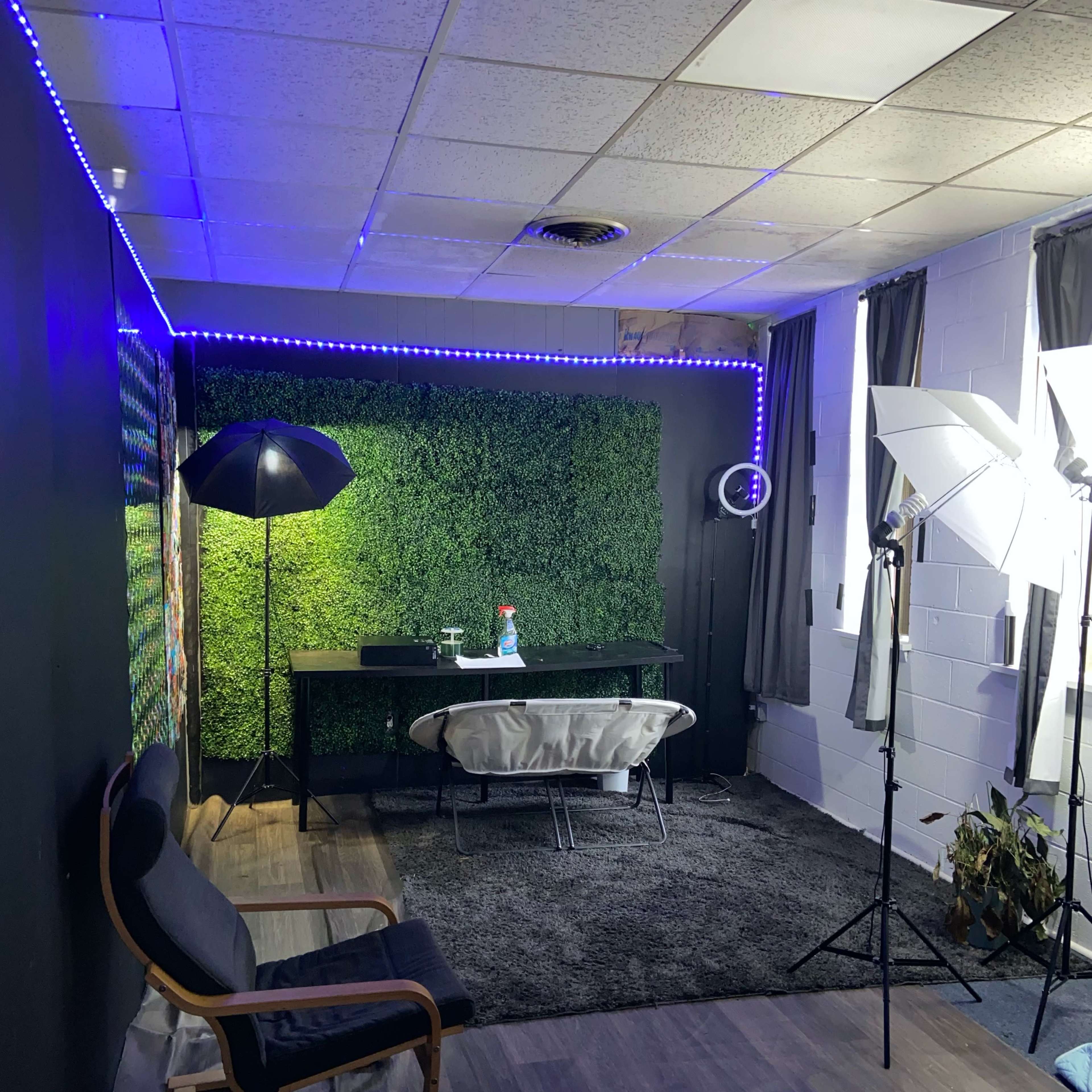 A small studio space with a green wall, a black desk, and photography lighting equipment.