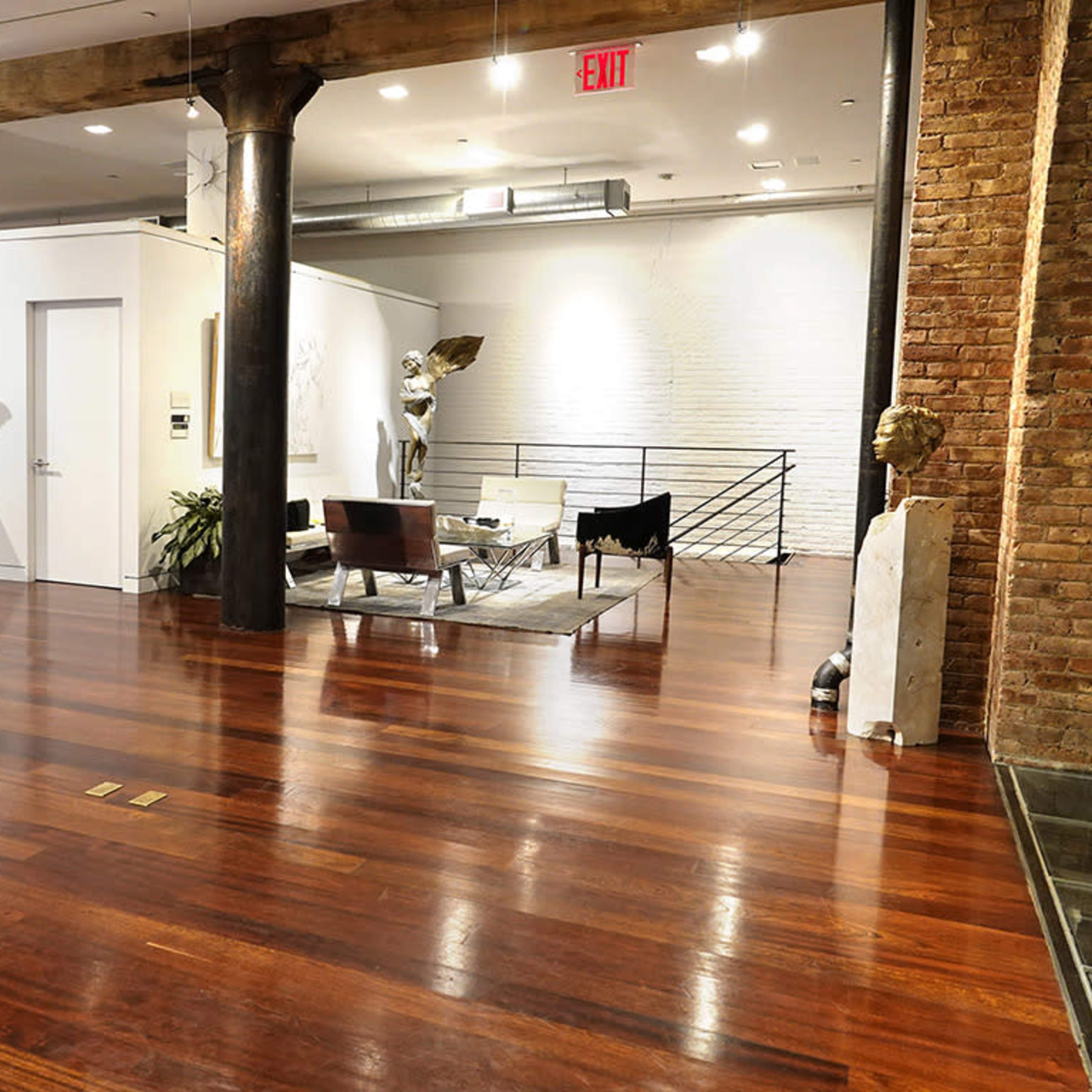 A modern art gallery with polished wooden floors, featuring sculptures and framed photographs on the walls, and a seating area in the center.