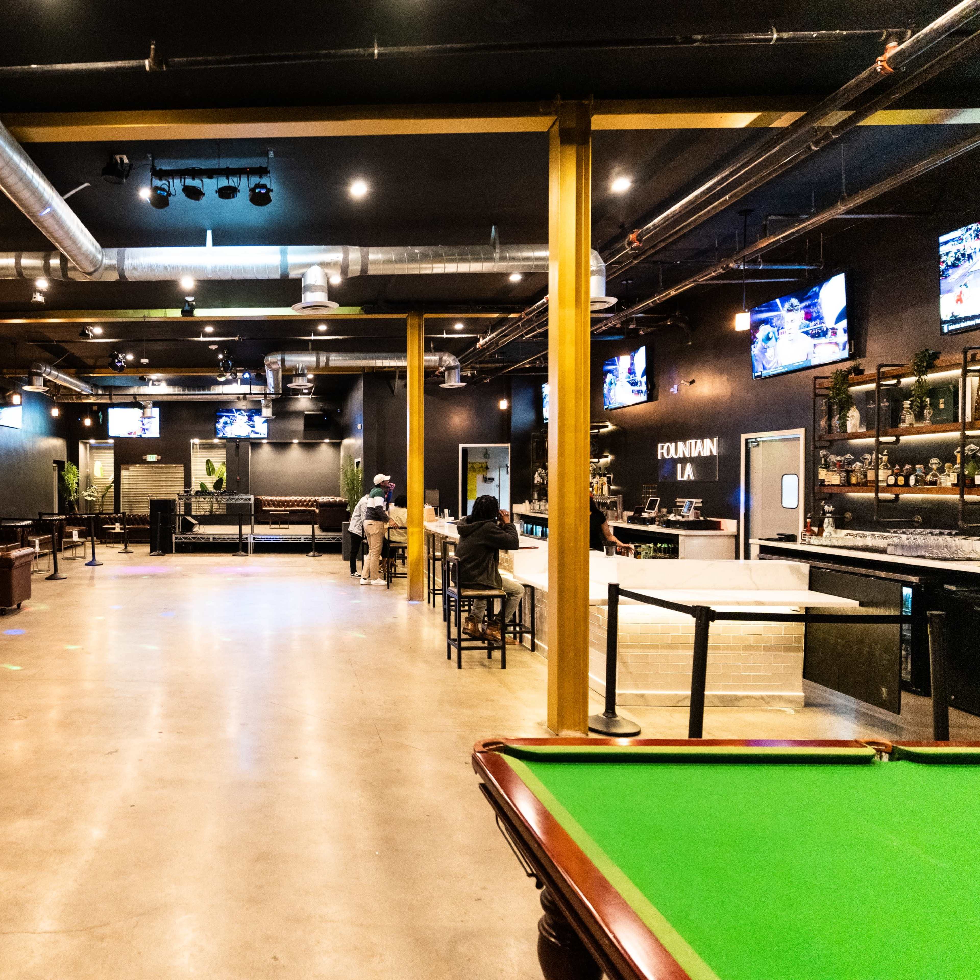 A spacious lounge area with a bar, pool table, and several seating arrangements, along with multiple screens mounted on the walls.