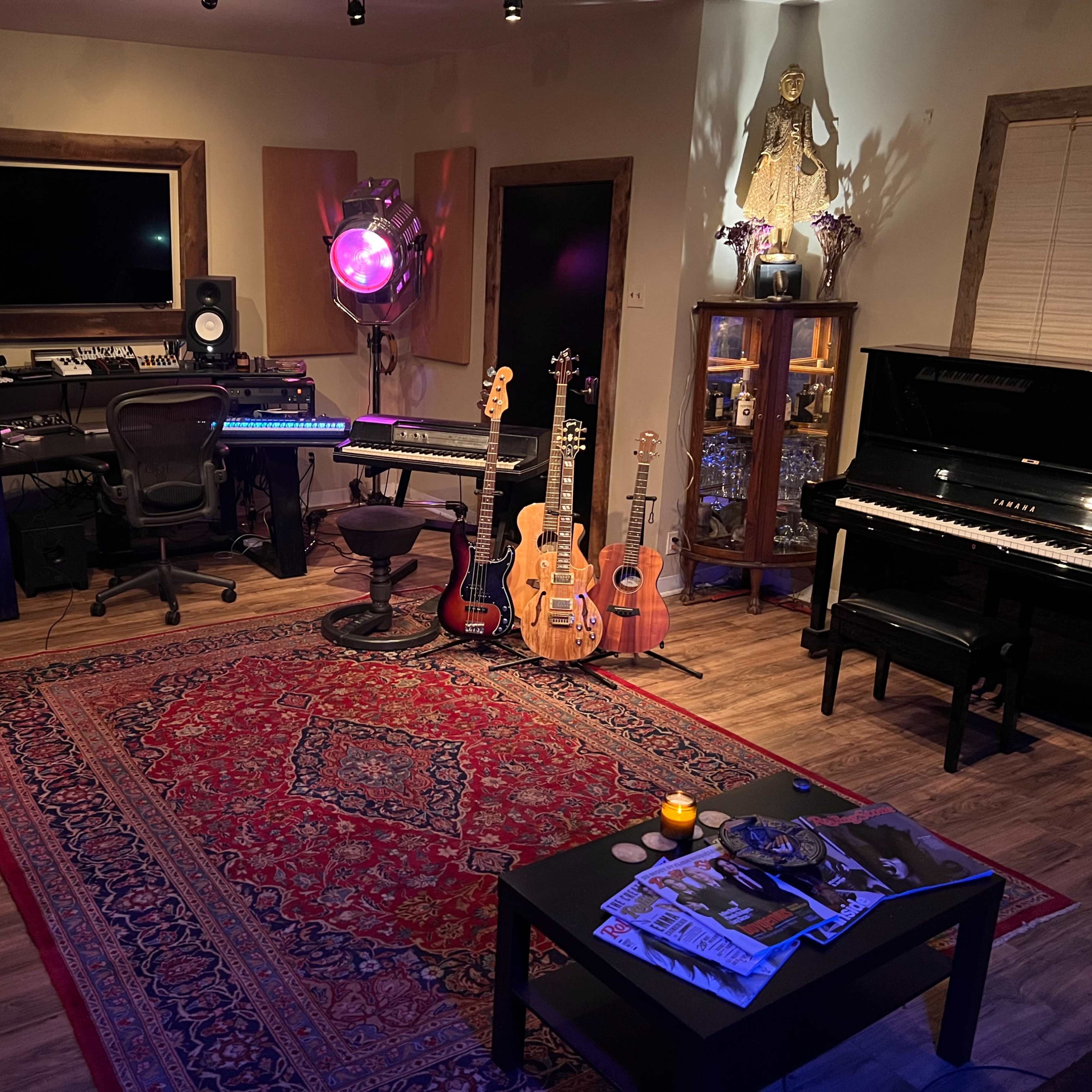A home music studio featuring various instruments, including guitars and a piano, surrounded by a decorative rug and a section with studio equipment.