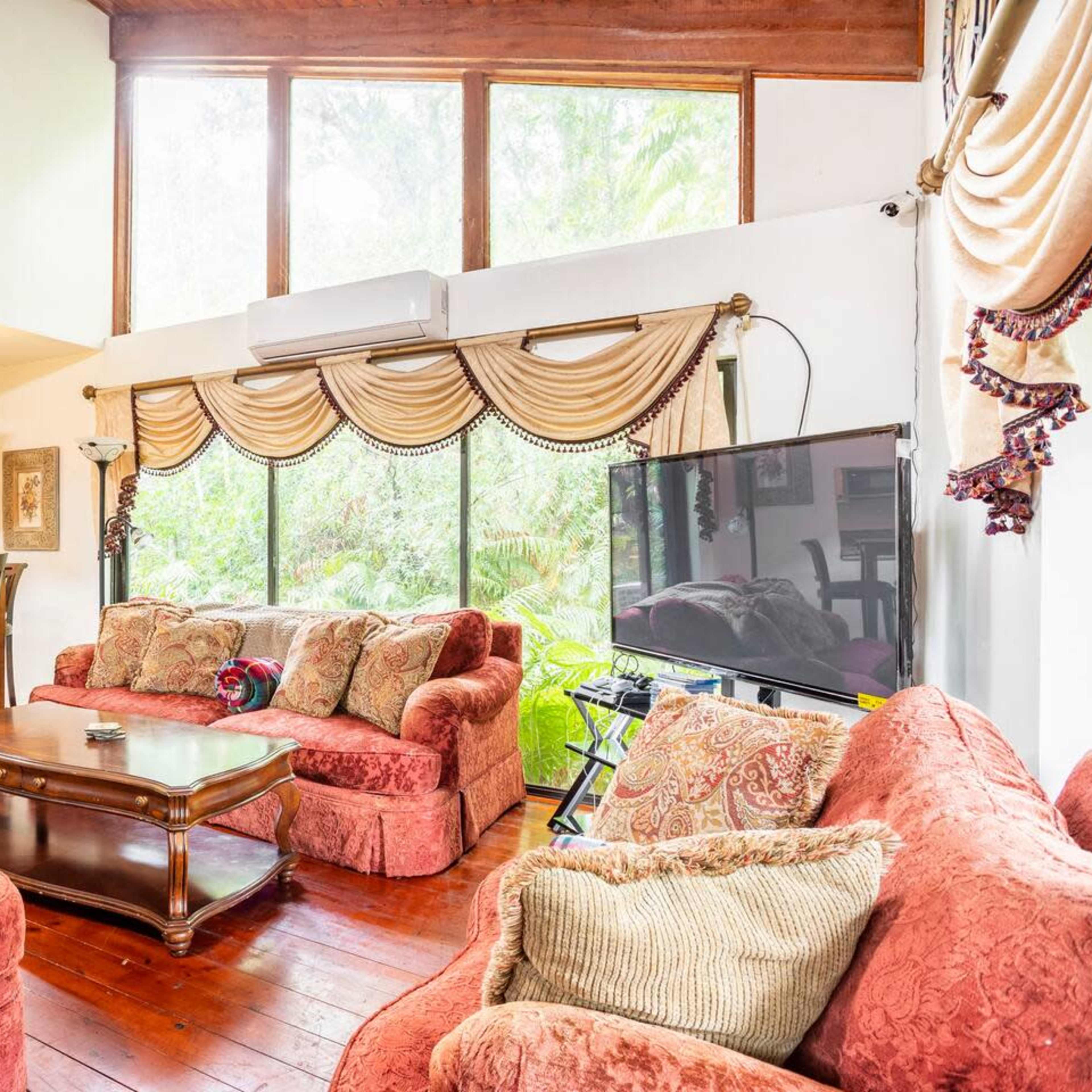 A living room with red upholstered sofas, a wooden coffee table, and large windows overlooking greenery.