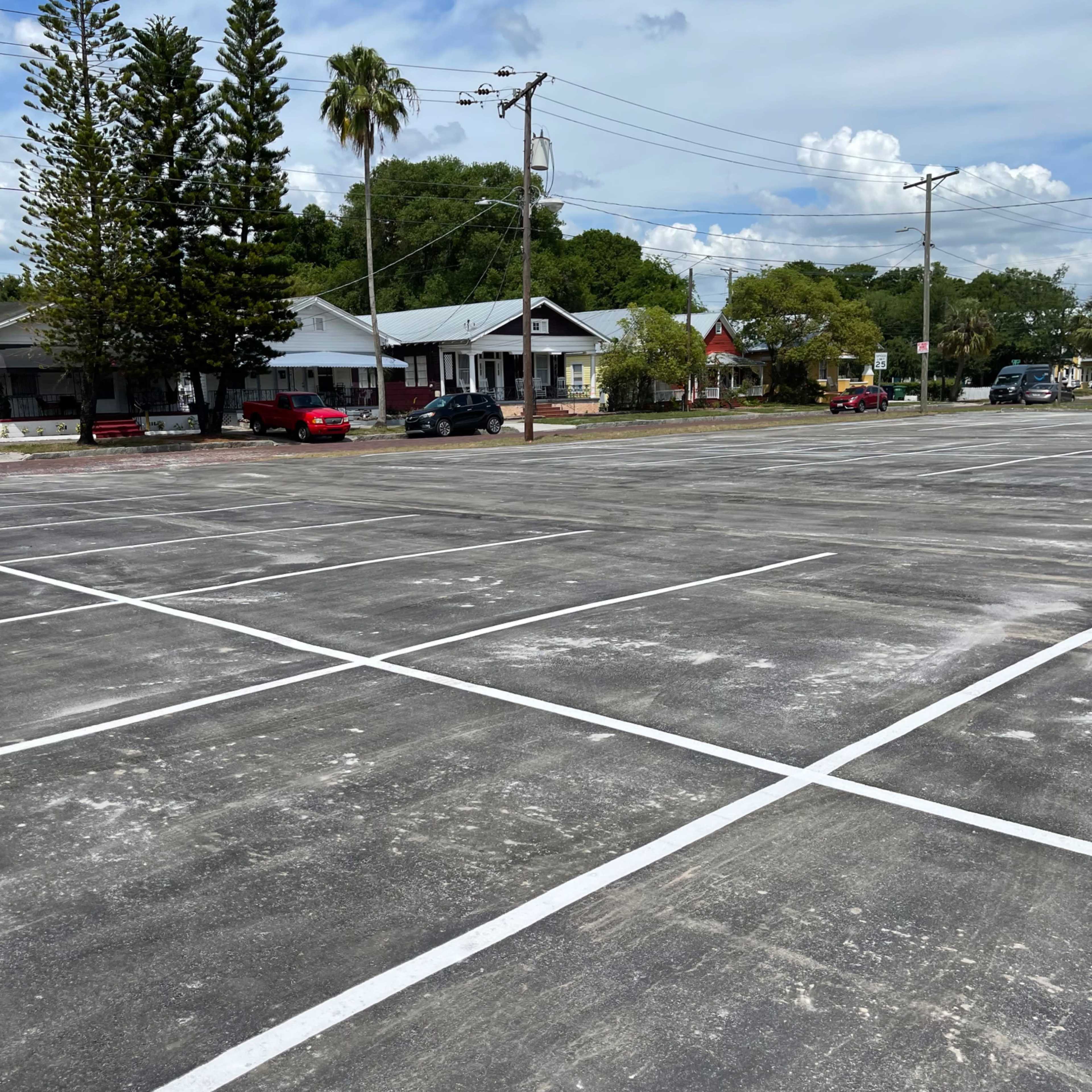 An empty parking lot with freshly marked lines, surrounded by a few houses and trees.