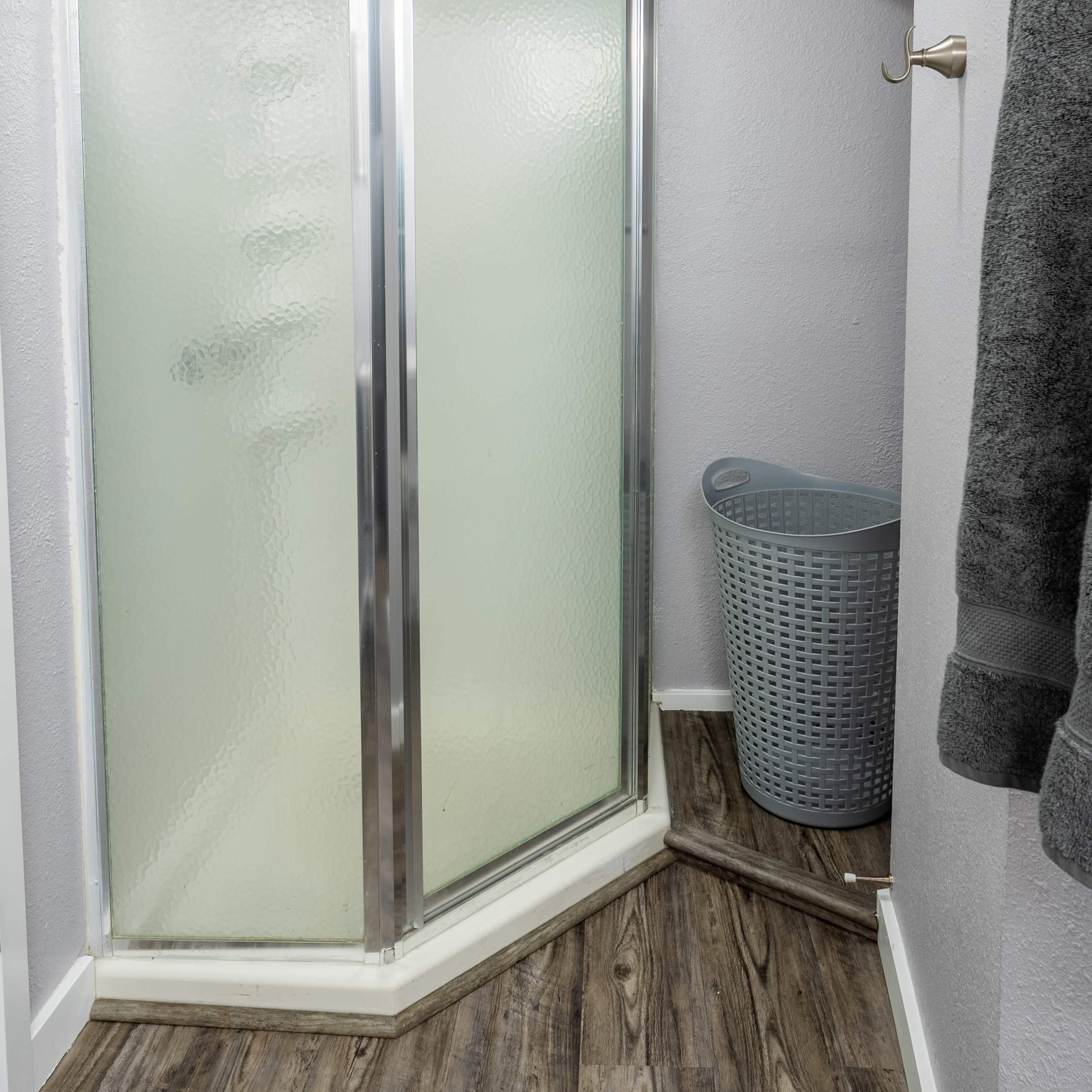 A small bathroom with a corner shower enclosure, a laundry basket, and a towel hanging on the wall.