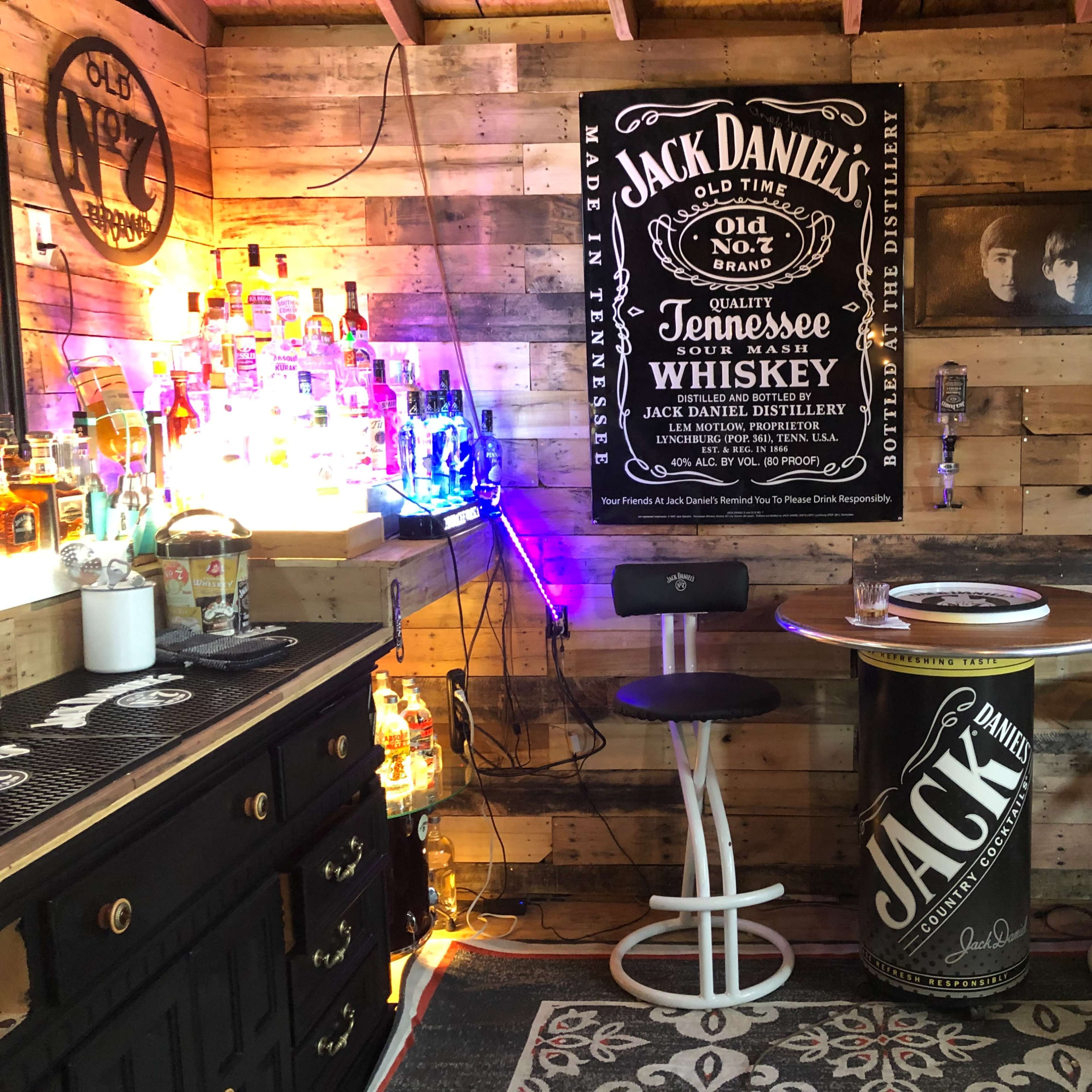 A rustic home bar featuring a wooden interior, a round bar table with stools, and various bottles of liquor displayed on shelves.