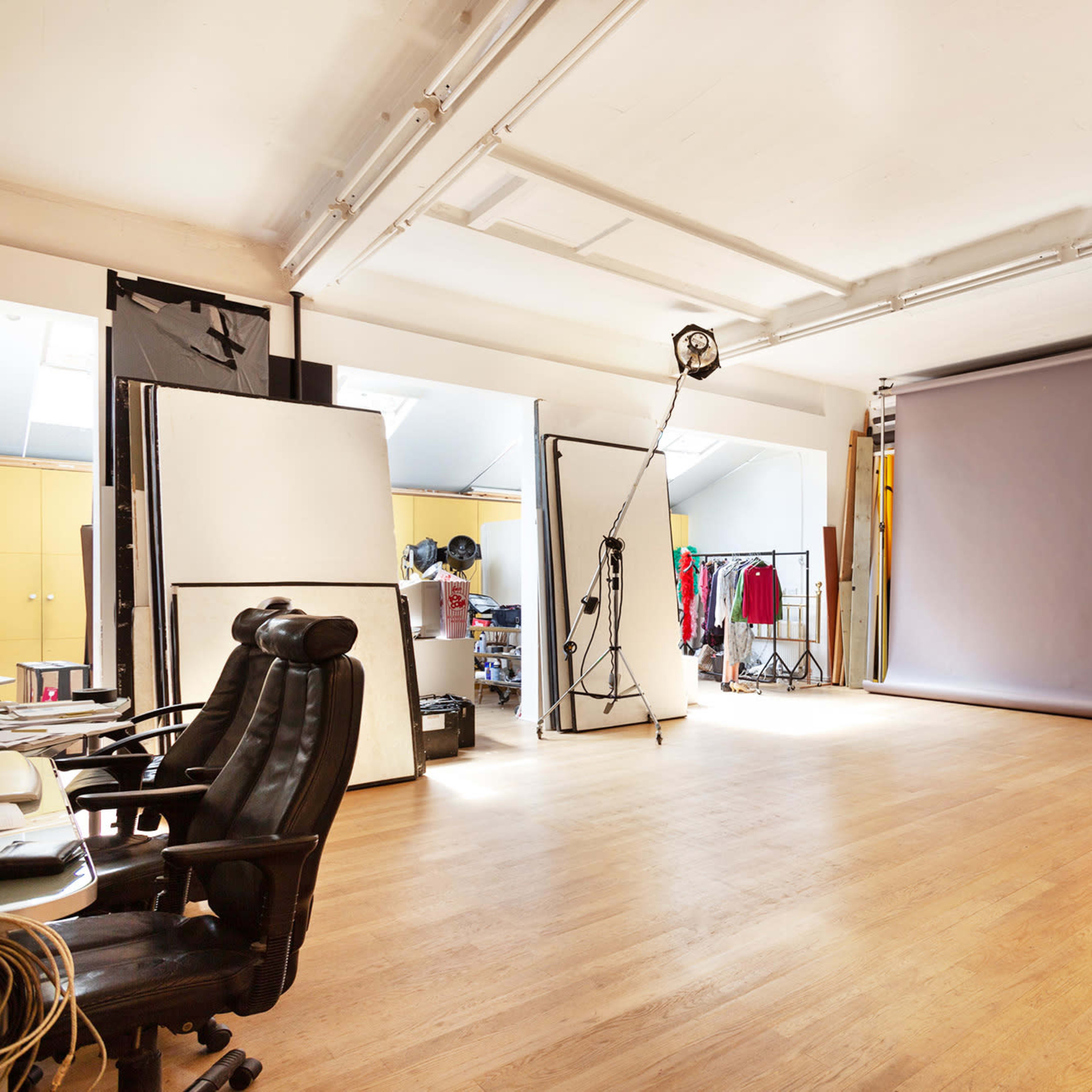 A spacious photography studio with a gray backdrop, lighting equipment, and various props and clothing racks in a well-organized setting.
