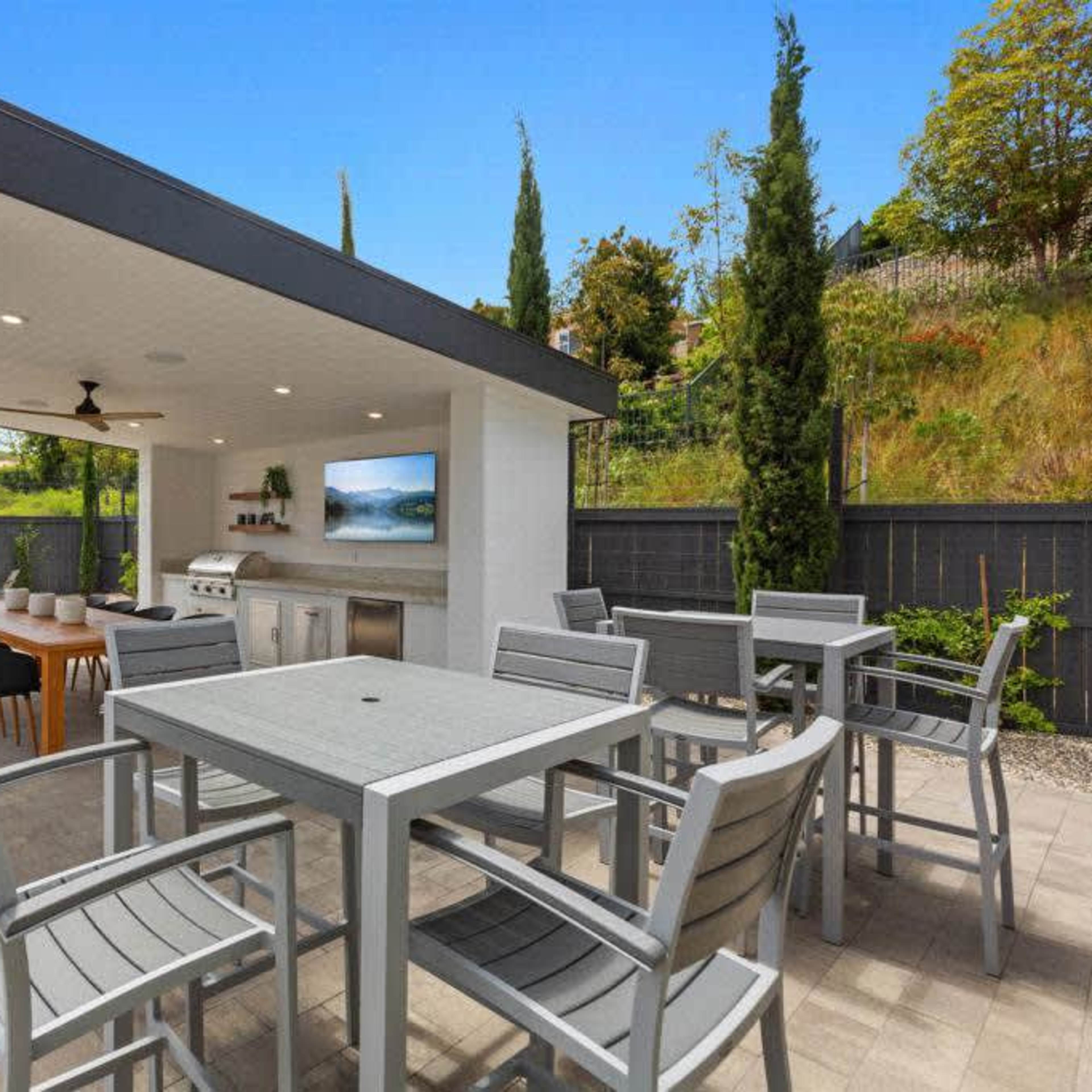 A modern outdoor patio area featuring a dining table, seating, and an outdoor kitchen with a grill.