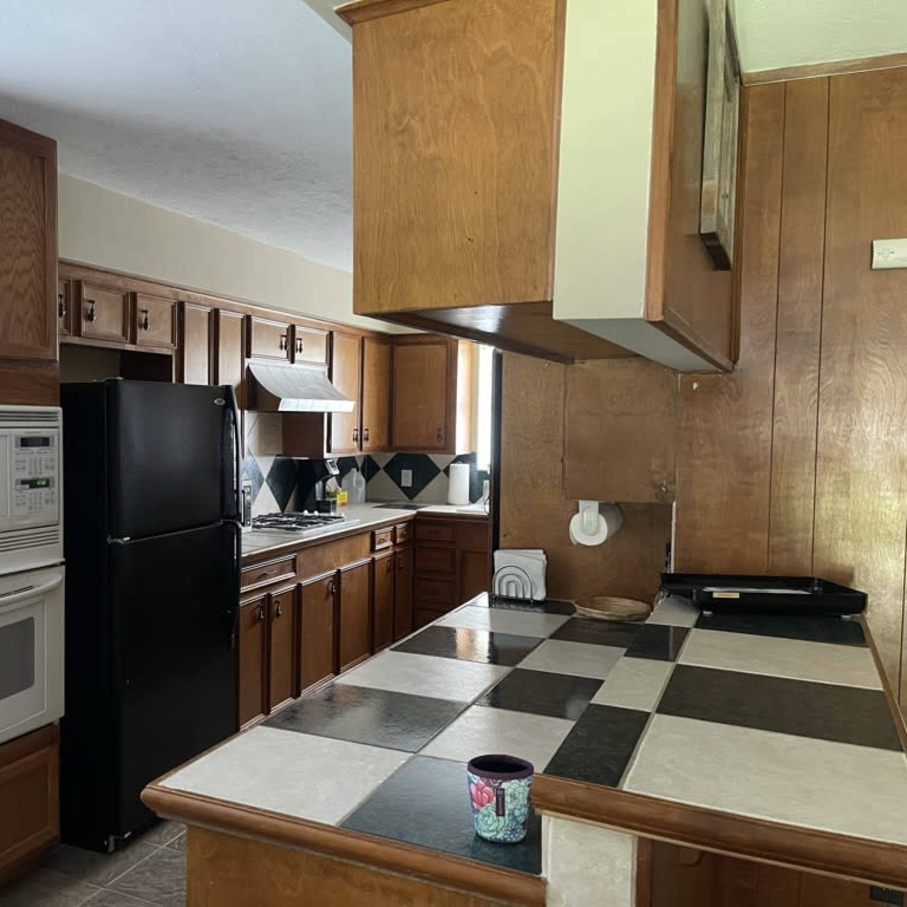 A kitchen with wooden cabinetry, a black refrigerator, an oven, and a checkered countertop.
