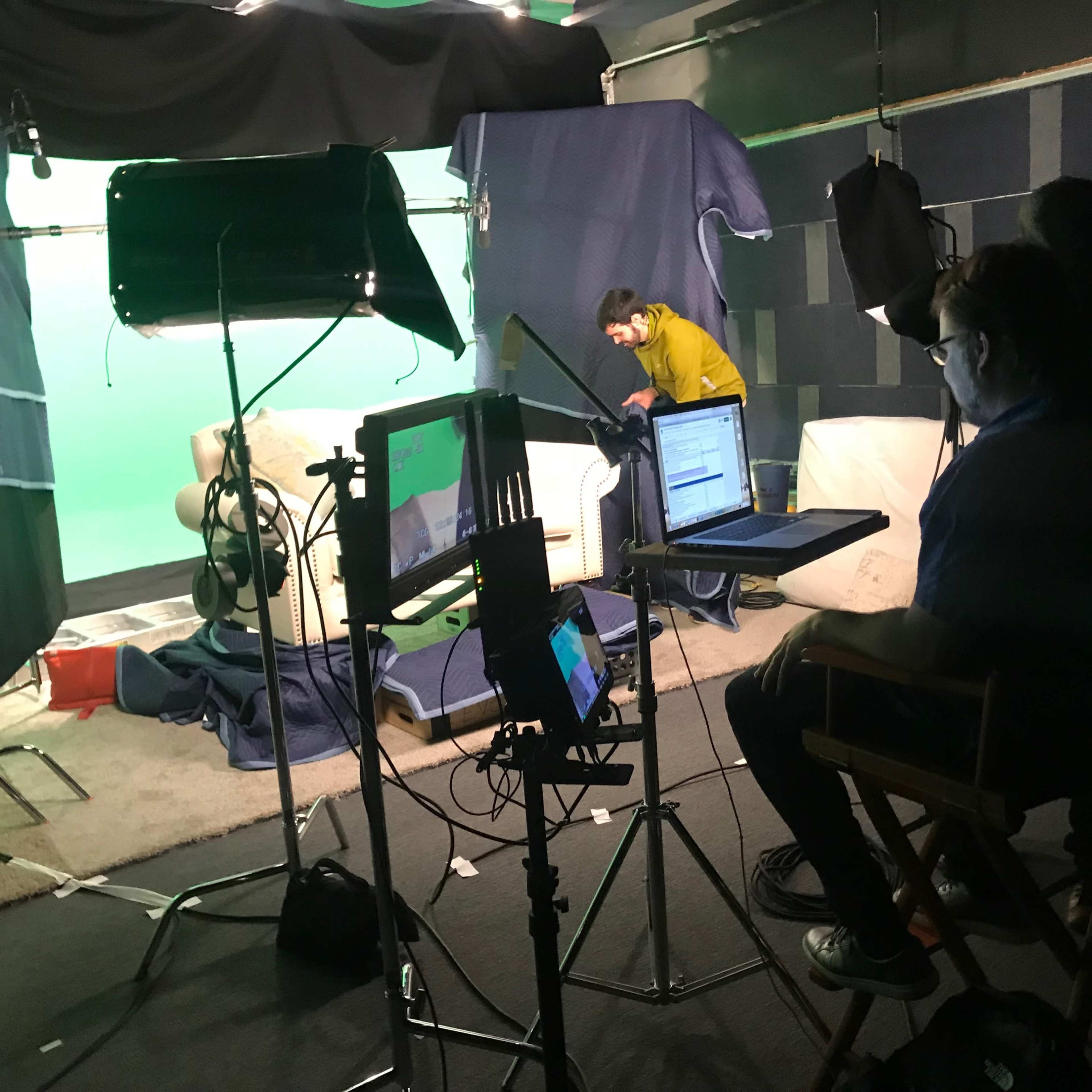 A film set is arranged with a green screen, lighting equipment, and crew members preparing a scene.