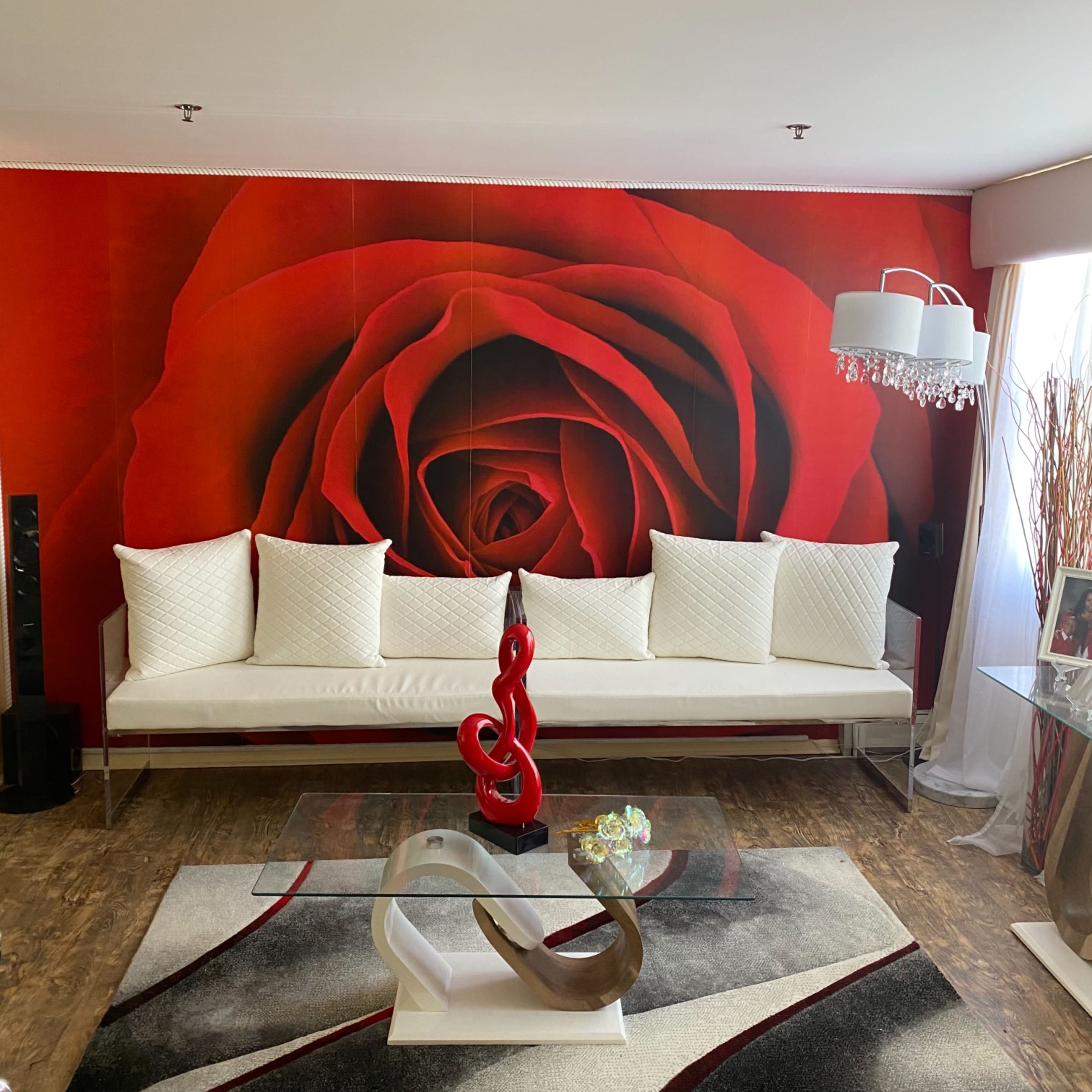 The living room features a large red rose mural, a white couch with decorative cushions, a glass coffee table, and a decorative sculpture on a patterned rug.