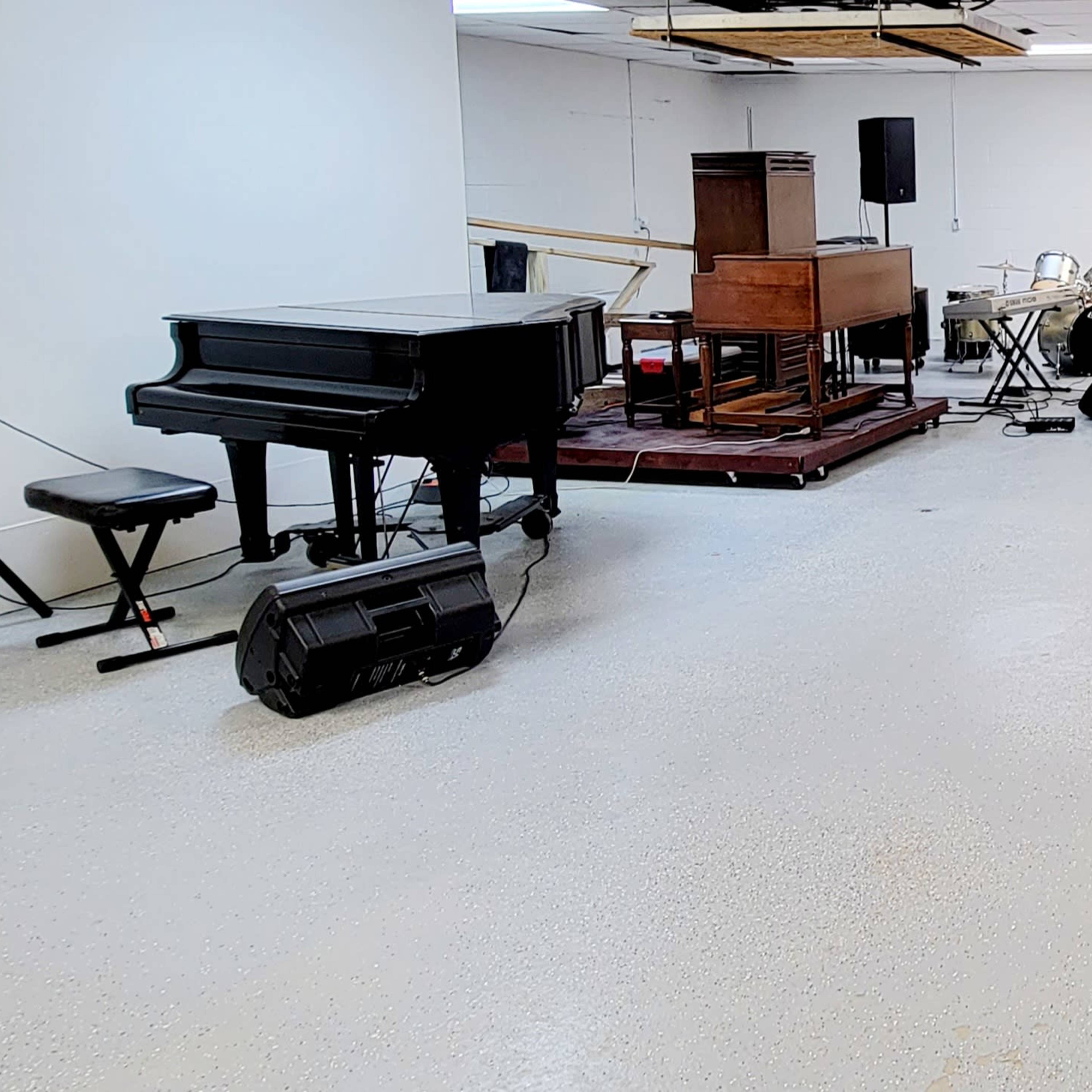 A spacious, empty room featuring a grand piano, a vintage organ, and several microphones on stands.