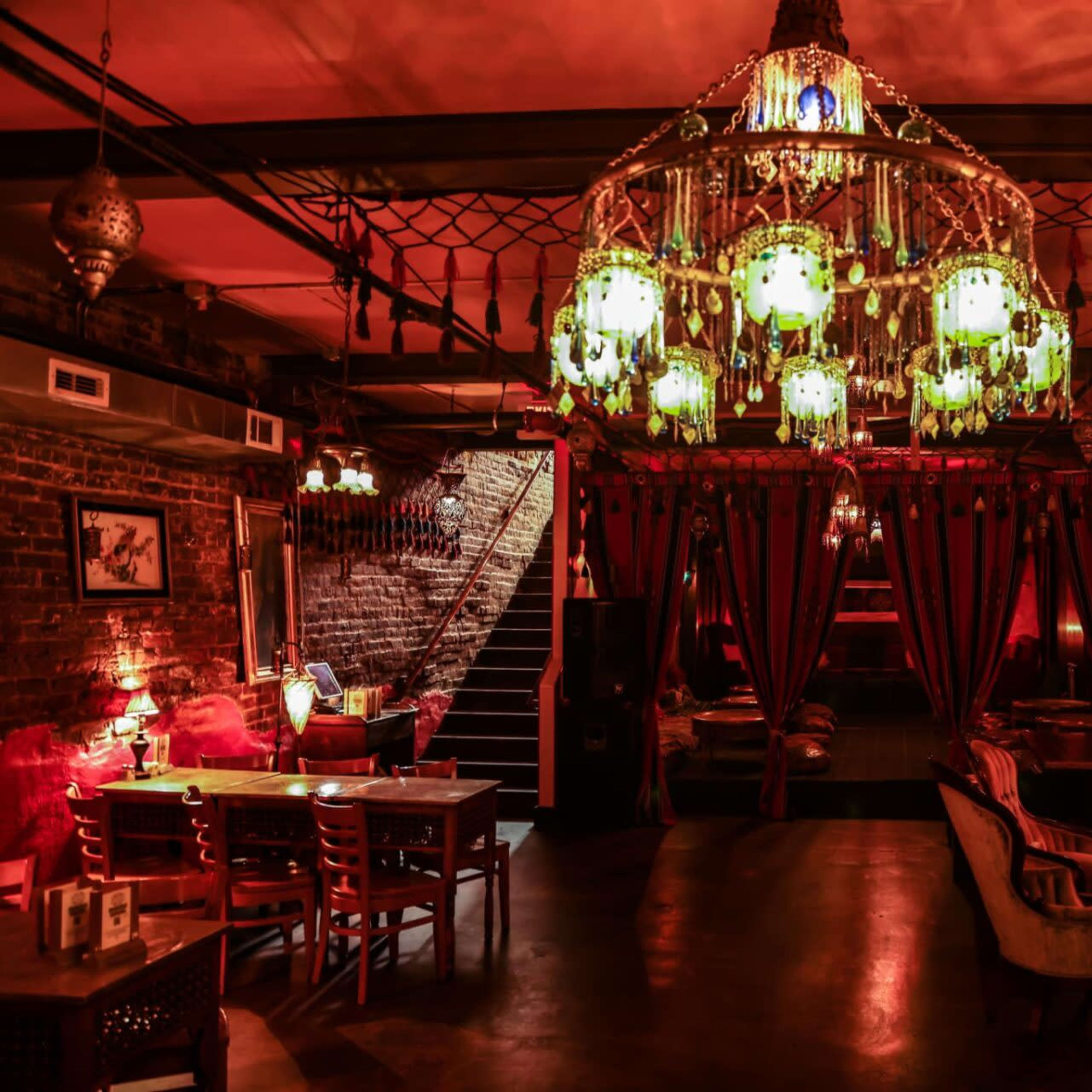 An elegantly designed restaurant interior featuring a large chandelier, vintage furnishings, and warm lighting.