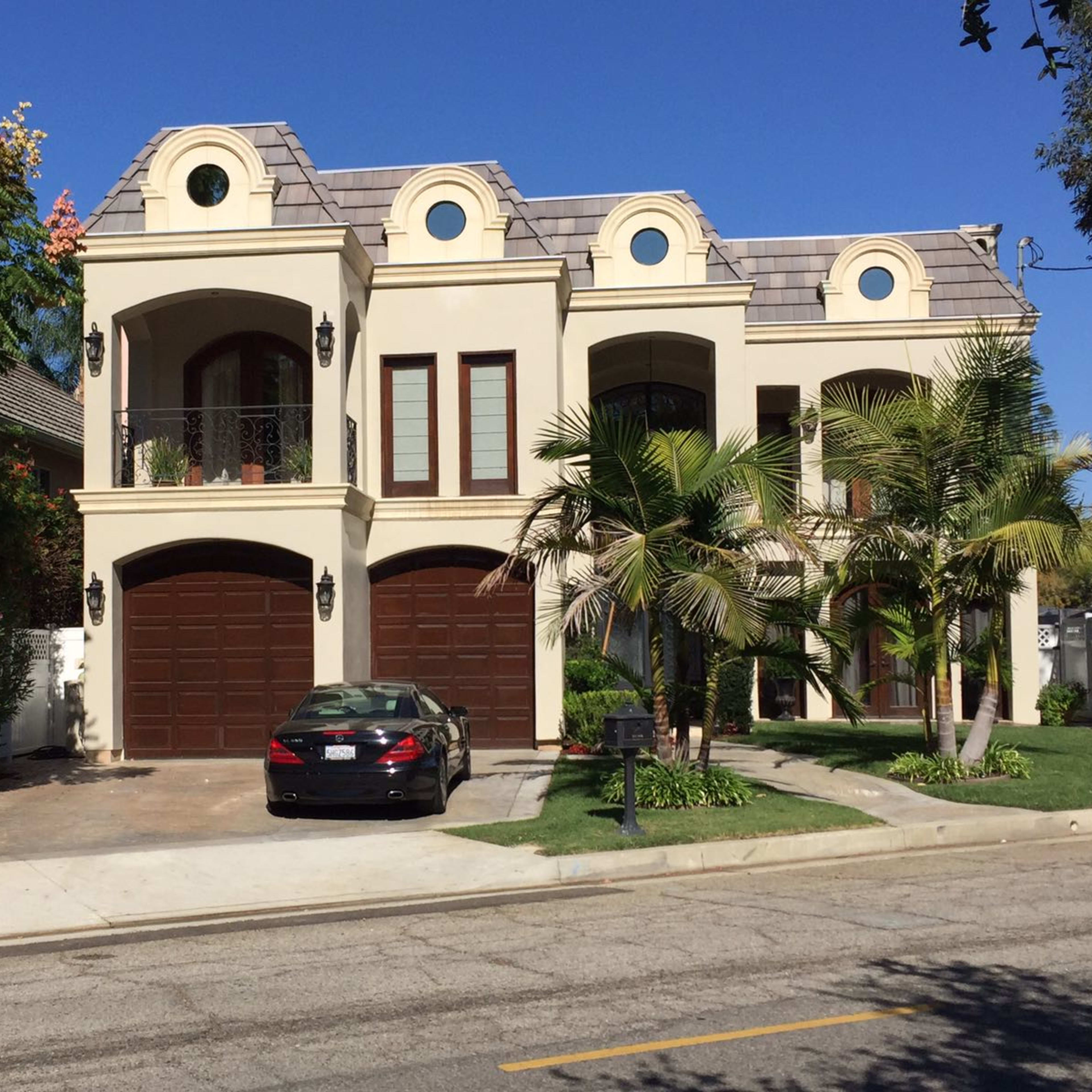 A large, two-story house with a tile roof and a dark sedan parked in front of the garage.