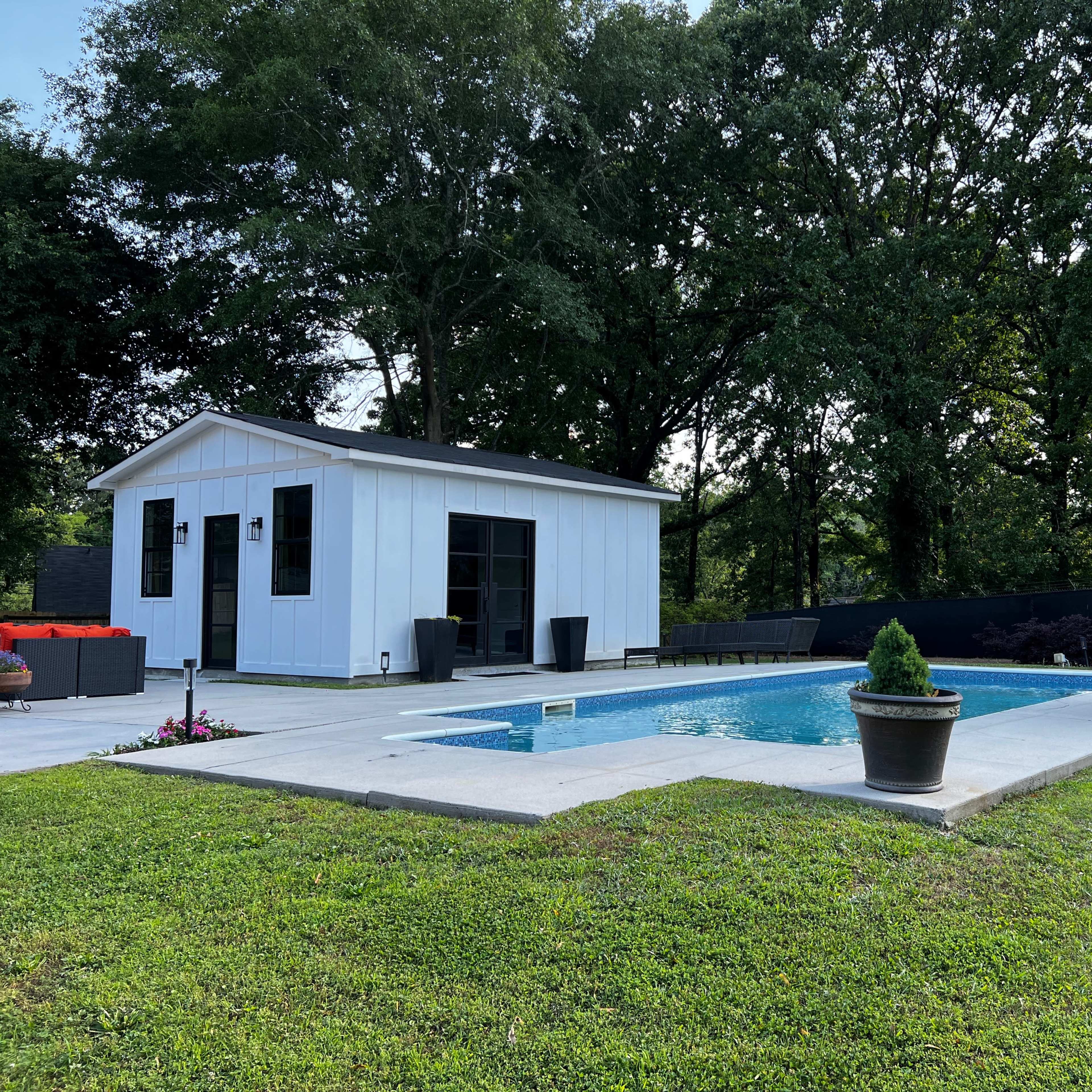 A backyard with a rectangular swimming pool, a small white building, and landscaped grass areas.
