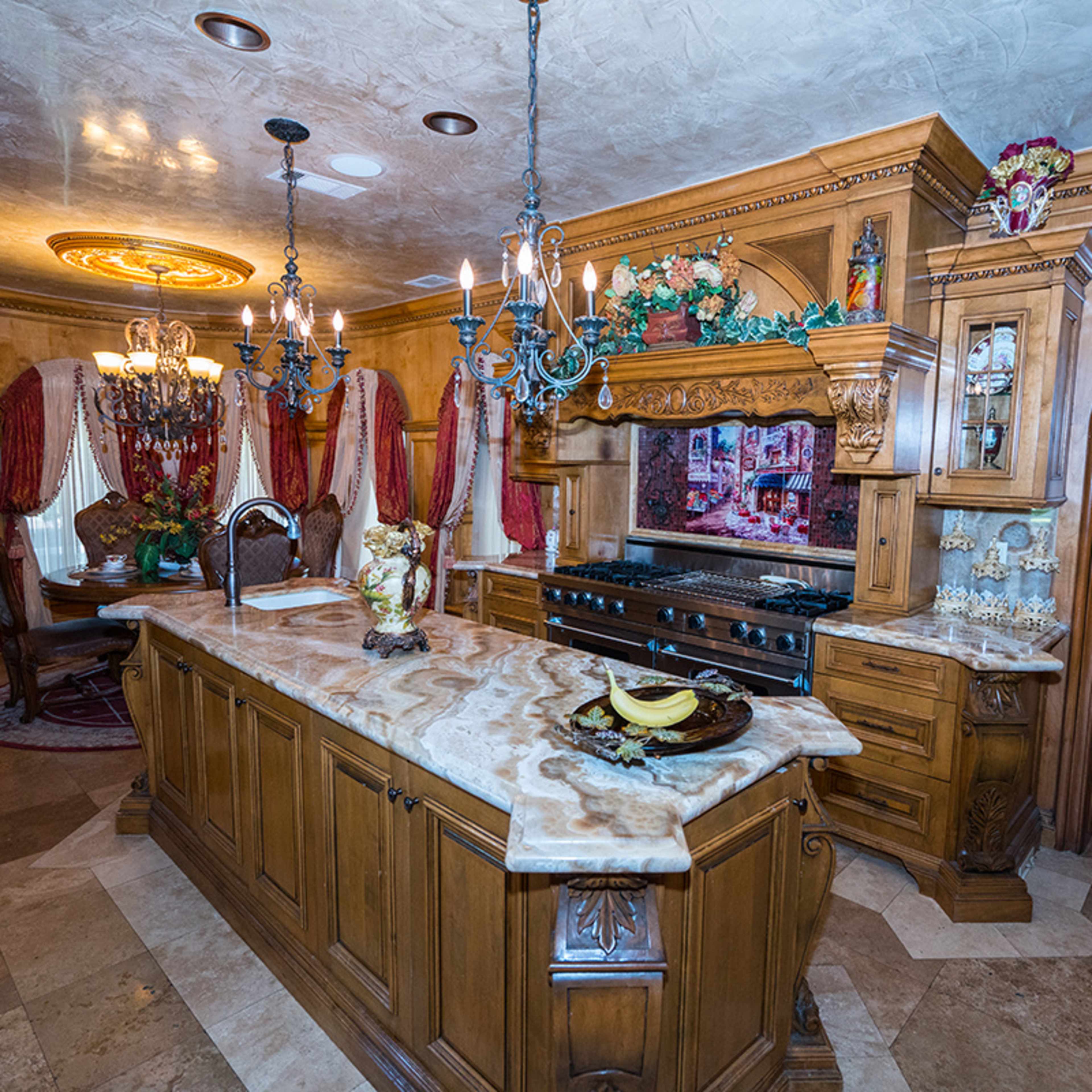 A luxurious kitchen featuring ornate wooden cabinetry, a large island with a marble countertop, and ornate chandeliers.
