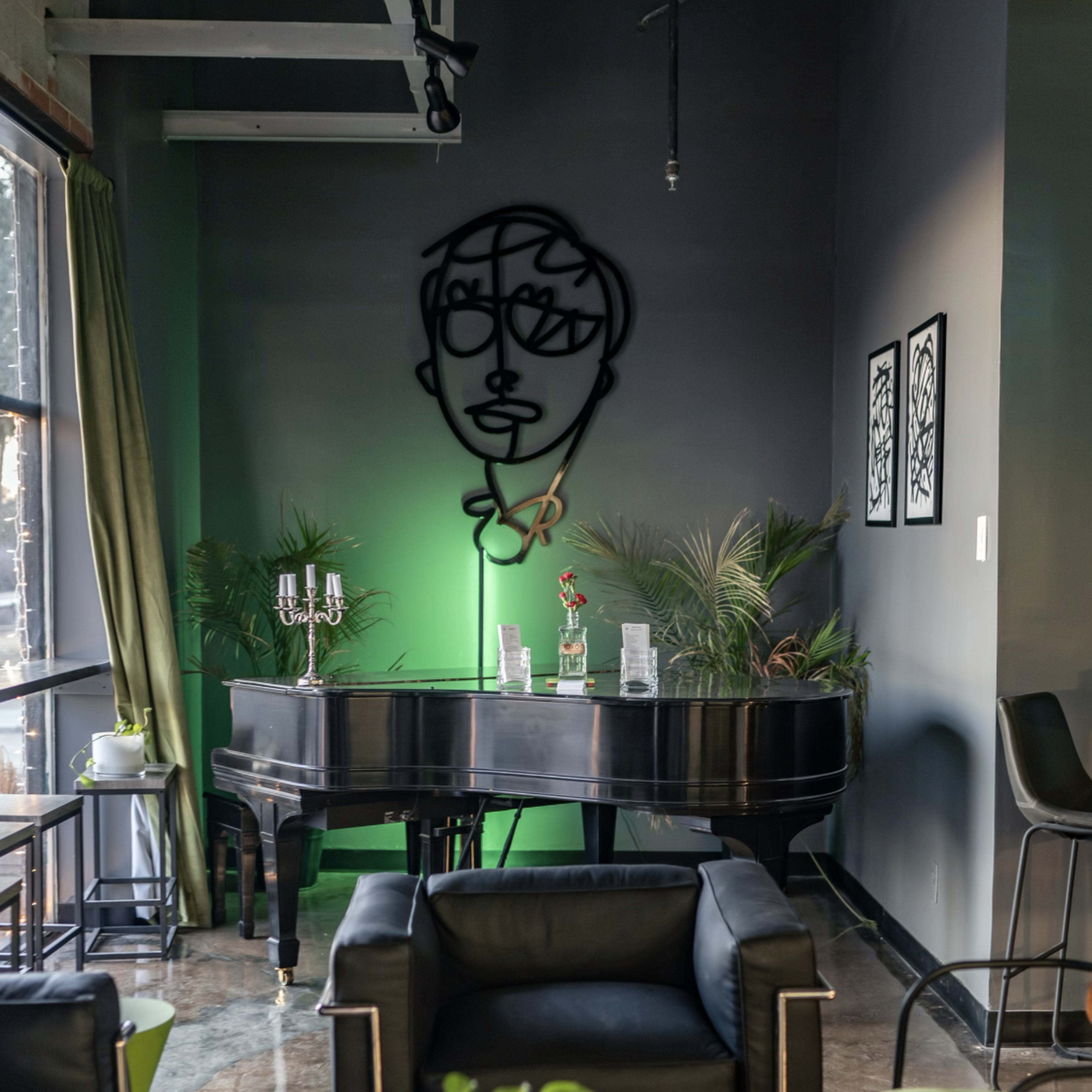 A grand piano sits against a dark wall, surrounded by plants and modern furniture in a stylish interior space.